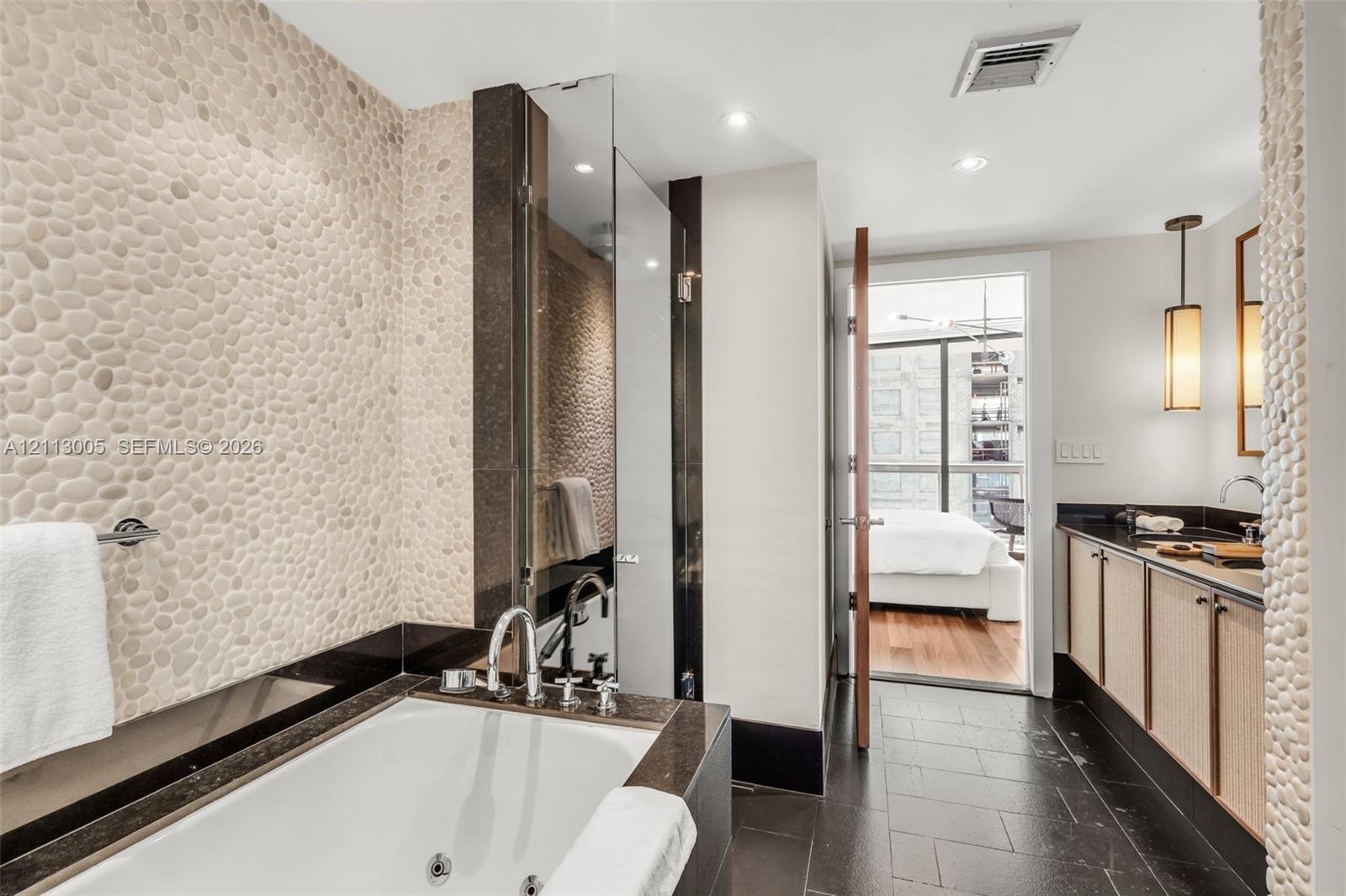 Bathroom featuring a deep soaking jetted tub, pebble-textured wall tiling, dark stone vanity countertop, slate tile flooring, and integrated pendant l