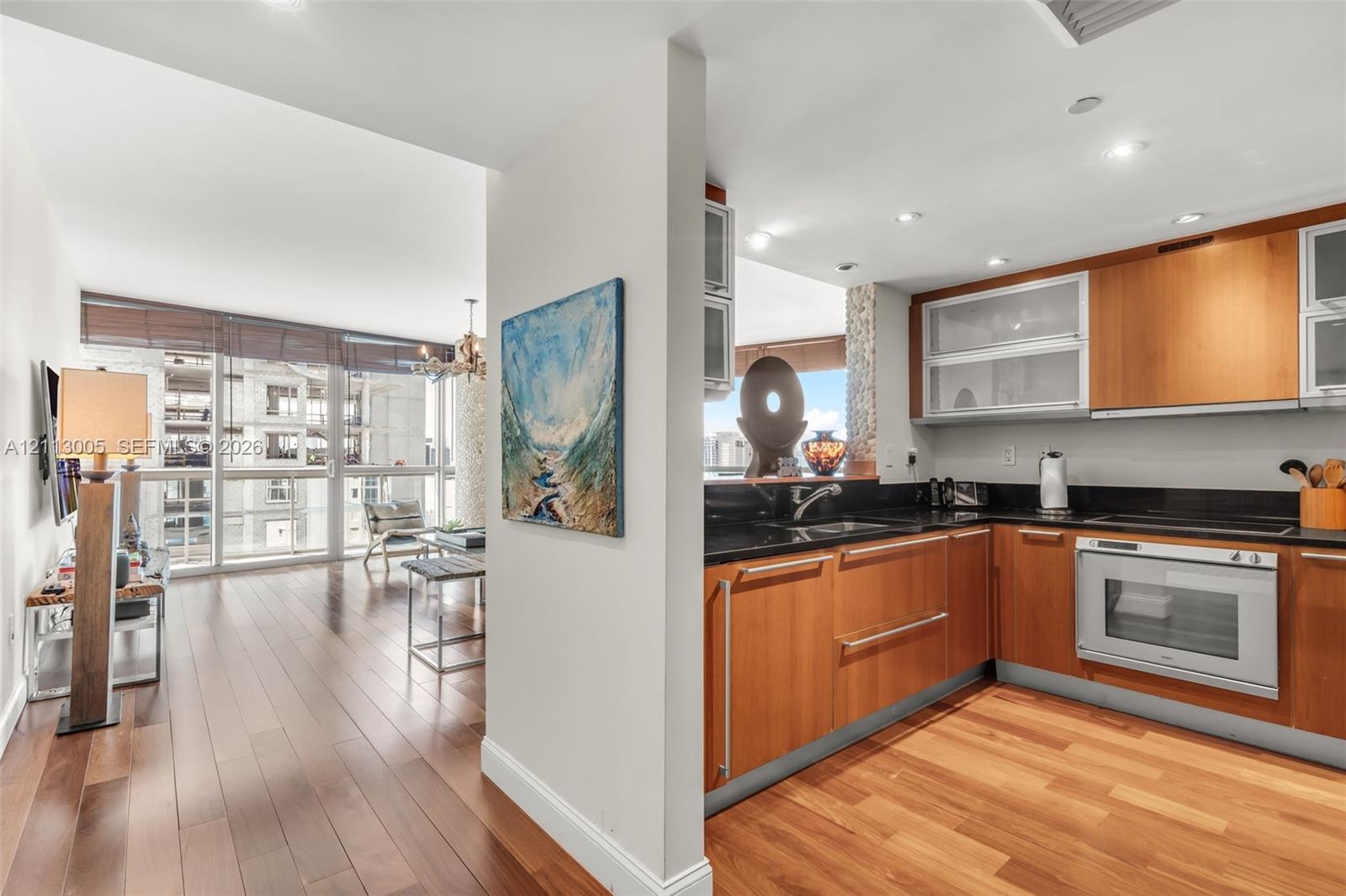 Kitchen featuring wood-finish cabinetry, dark stone-surface countertops, built-in oven, and recessed lighting, complemented by wood-finish flooring th