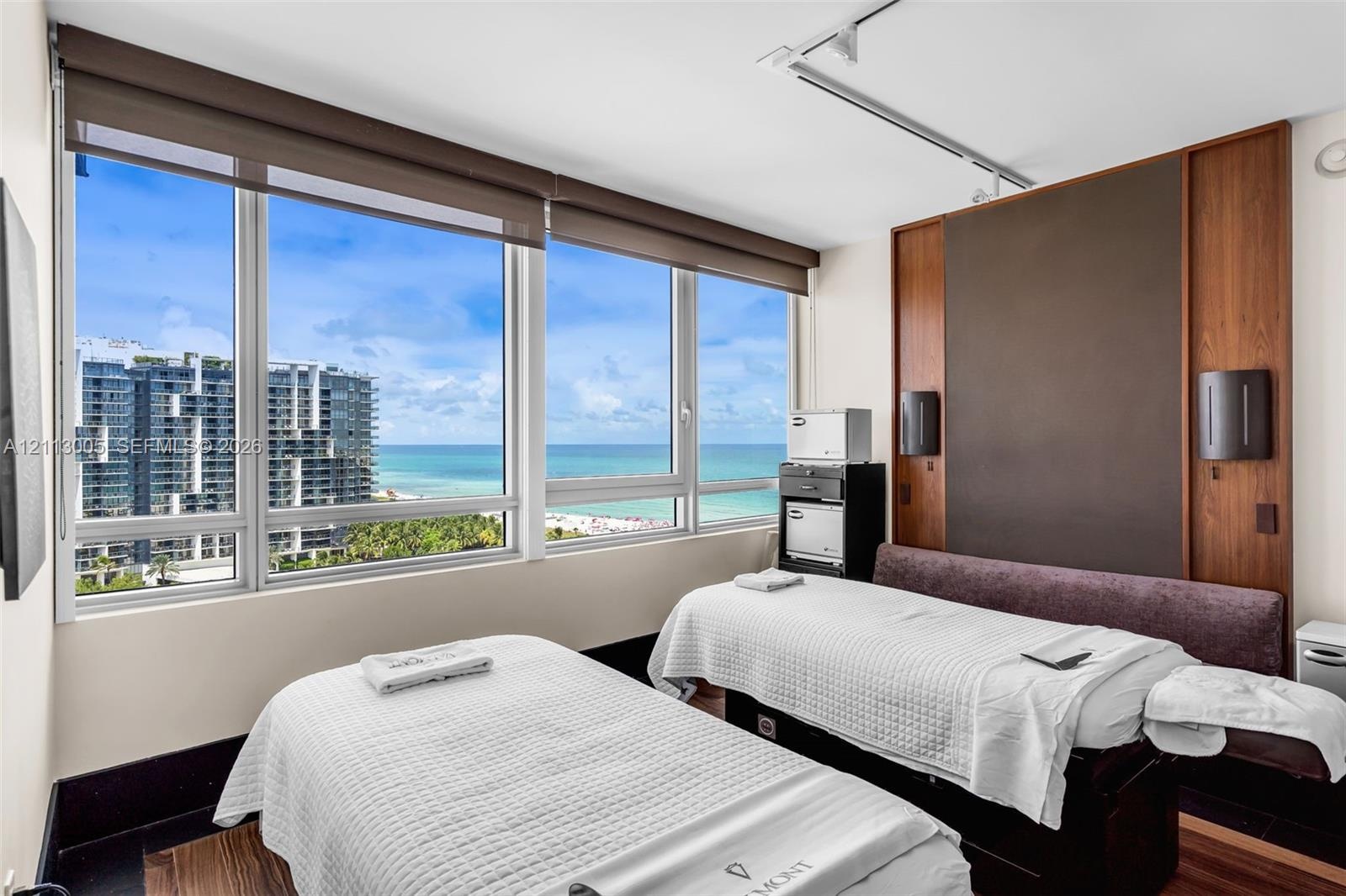 Floor-to-ceiling windows, wood-panel accent wall with built-in wall sconces, wood-finish flooring, and coastal scenery