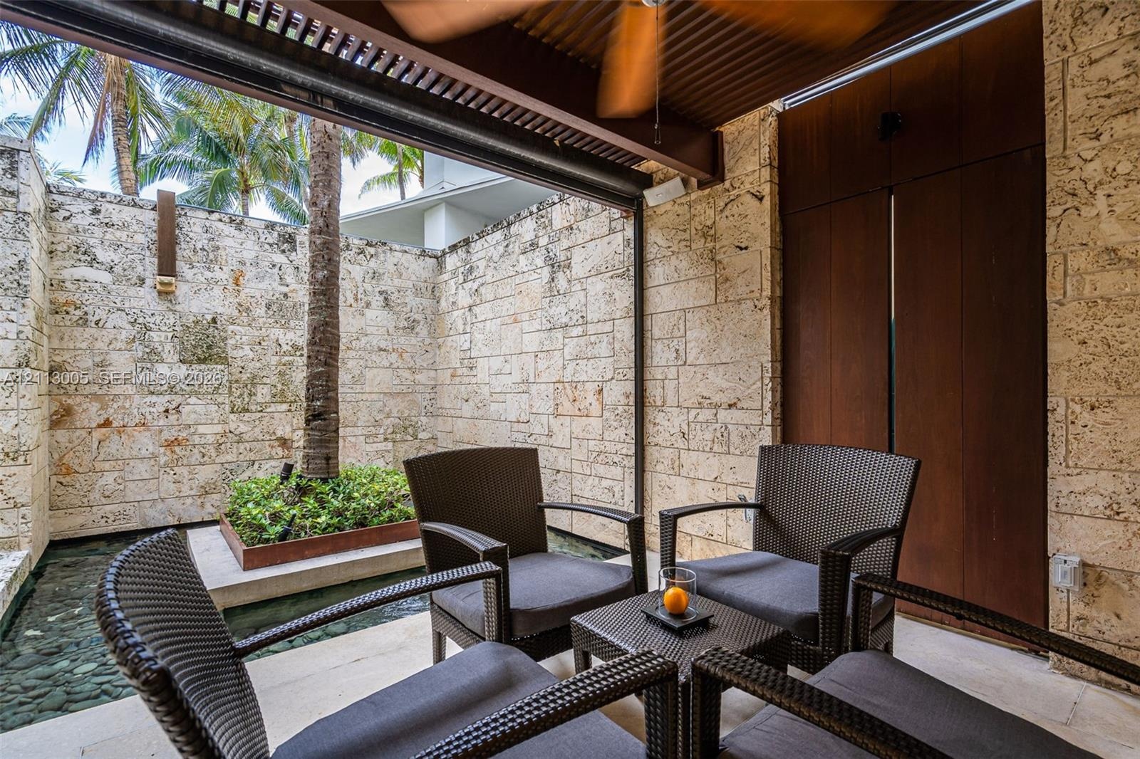 Covered patio featuring stacked stone walls, wood-paneled accents, a coffered ceiling with a mounted fan, and a built-in water feature with a raised g