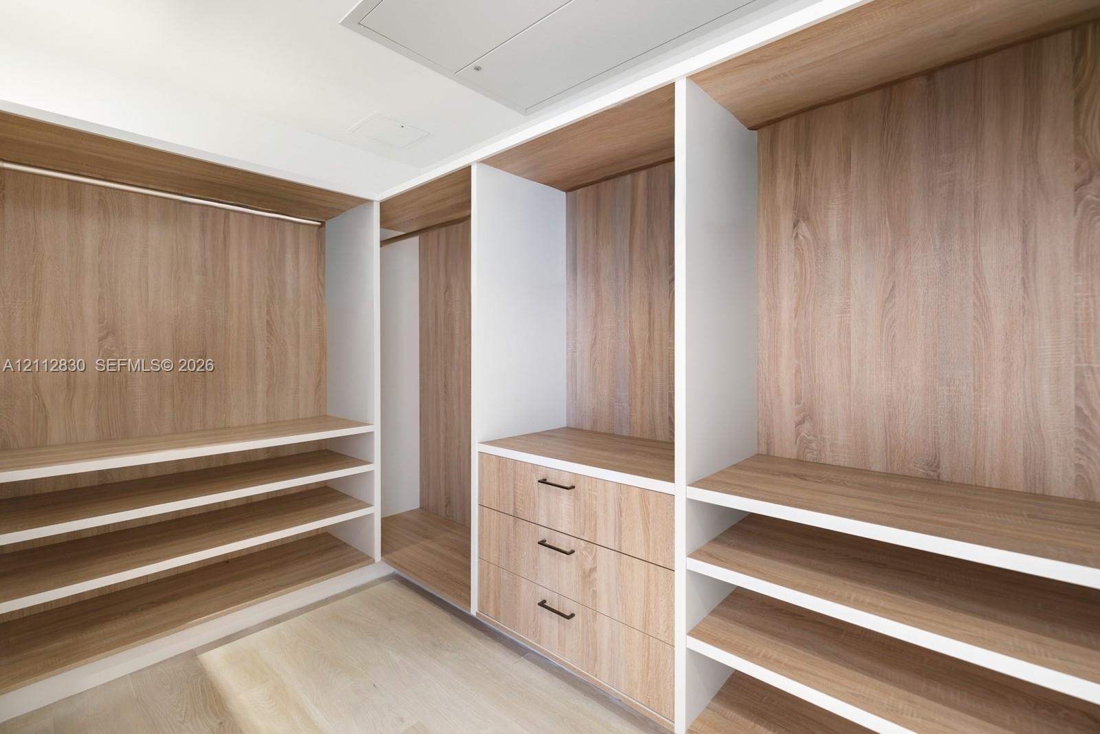 Custom walk-in closet featuring wood-finish cabinetry, built-in shelving, integrated hanging rods, and a three-drawer storage unit with matte black ha