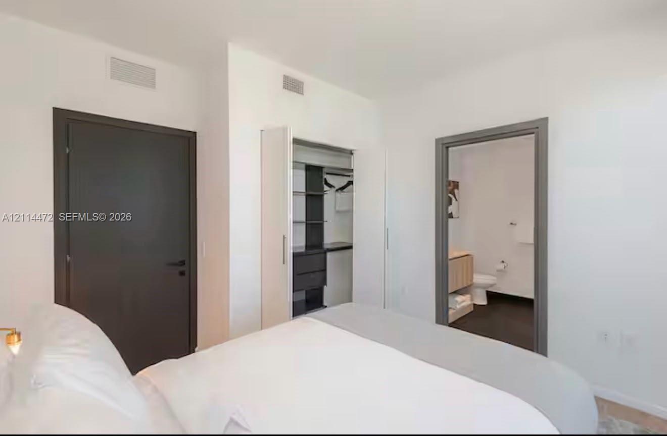 Neutral-toned bedroom featuring a dark solid-core door, built-in closet with integrated shelving, and a doorway showcasing a vanity with a light-finis