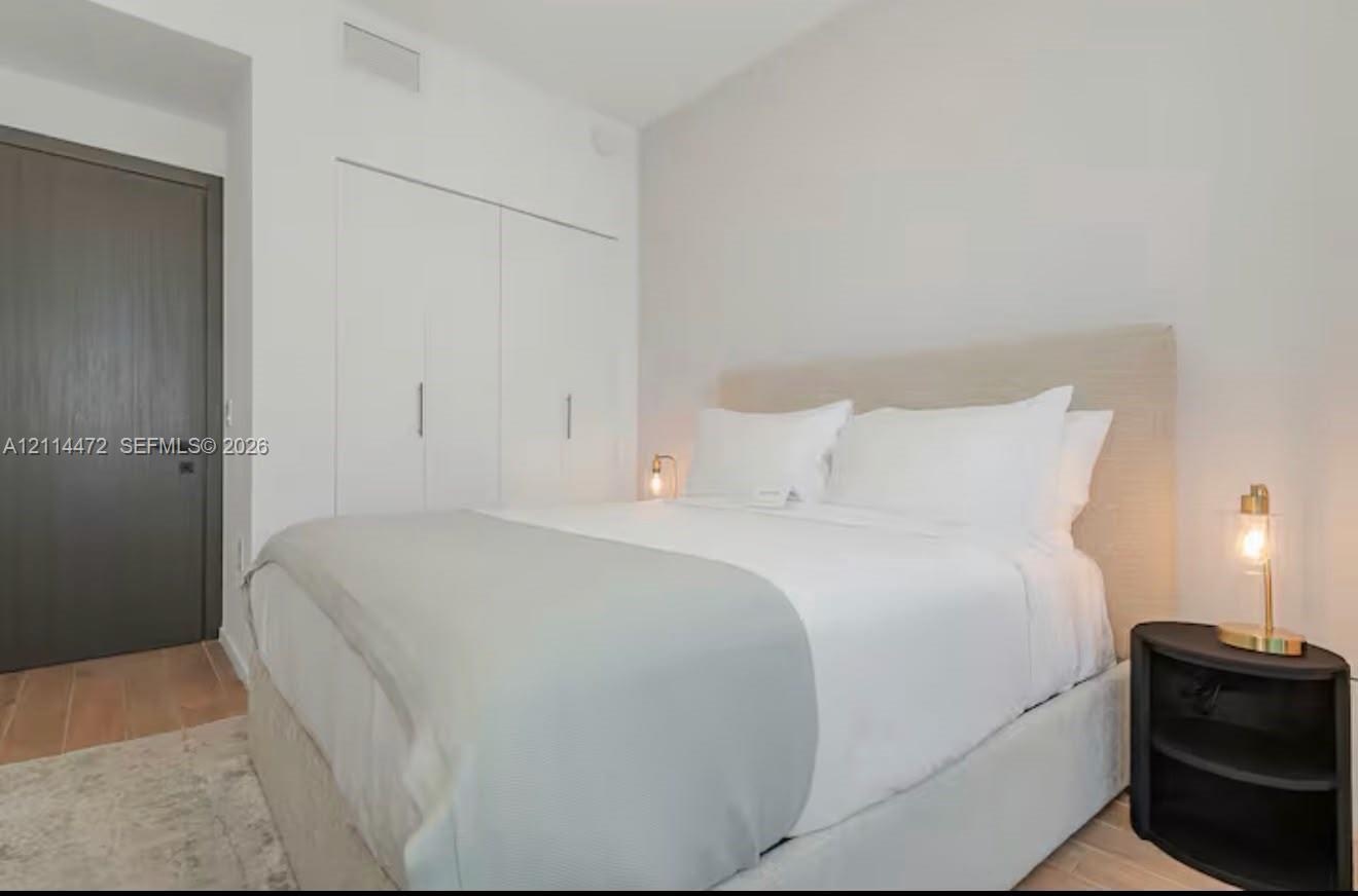 Wood-finish flooring, neutral walls, integrated full-height storage cabinetry with metallic hardware, and a solid-core charcoal interior door