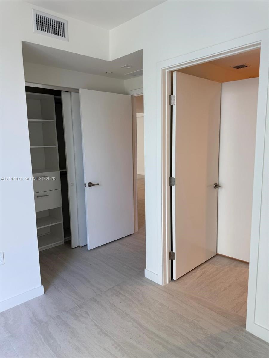 Interior space featuring wood-finish flooring, white solid-core doors with brushed nickel hardware, and built-in closet storage with integrated shelvi