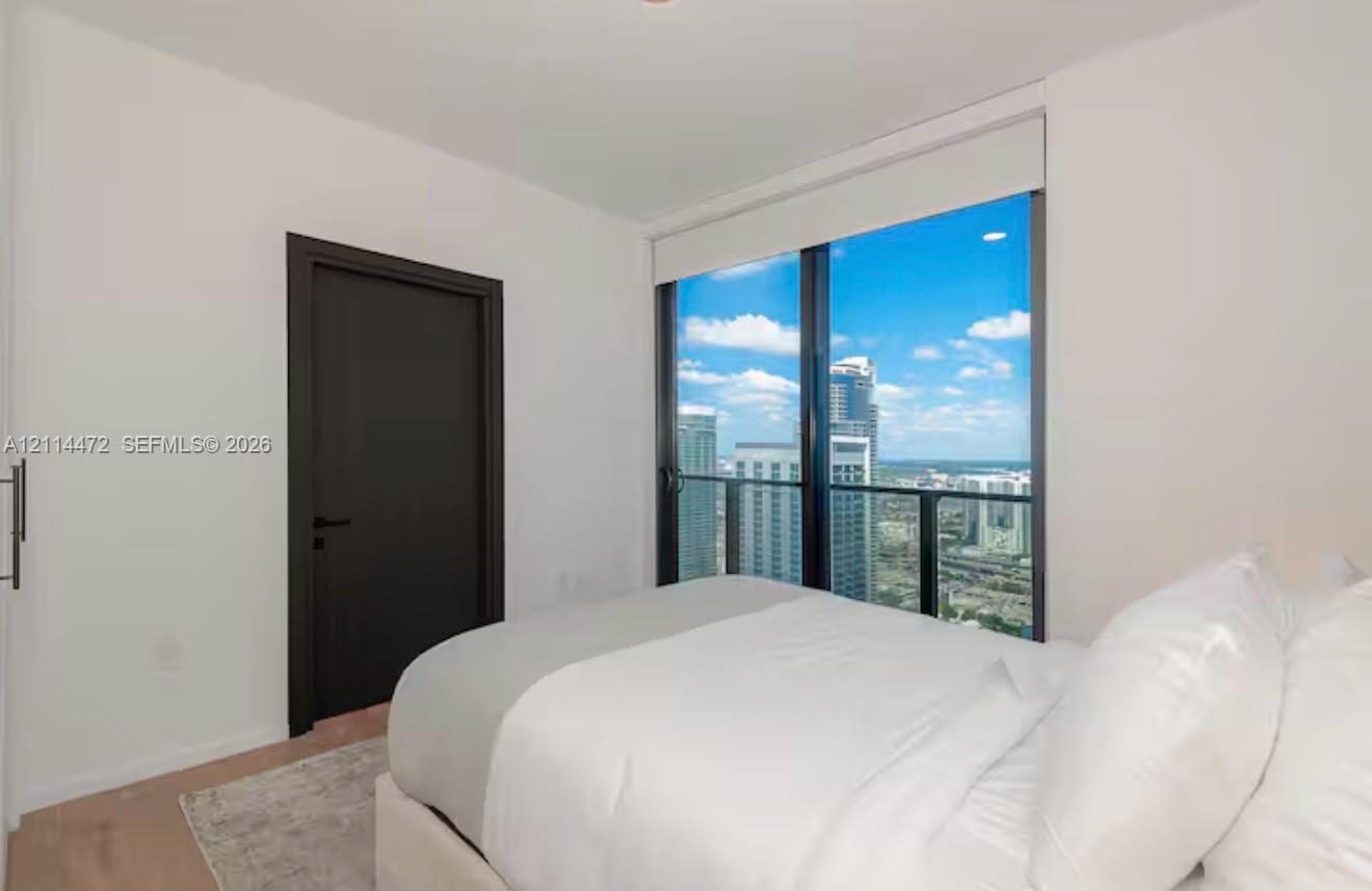 Floor-to-ceiling windows with expansive urban cityscape scenery, dark-finish interior door, recessed lighting, and light-tone wood-finish flooring