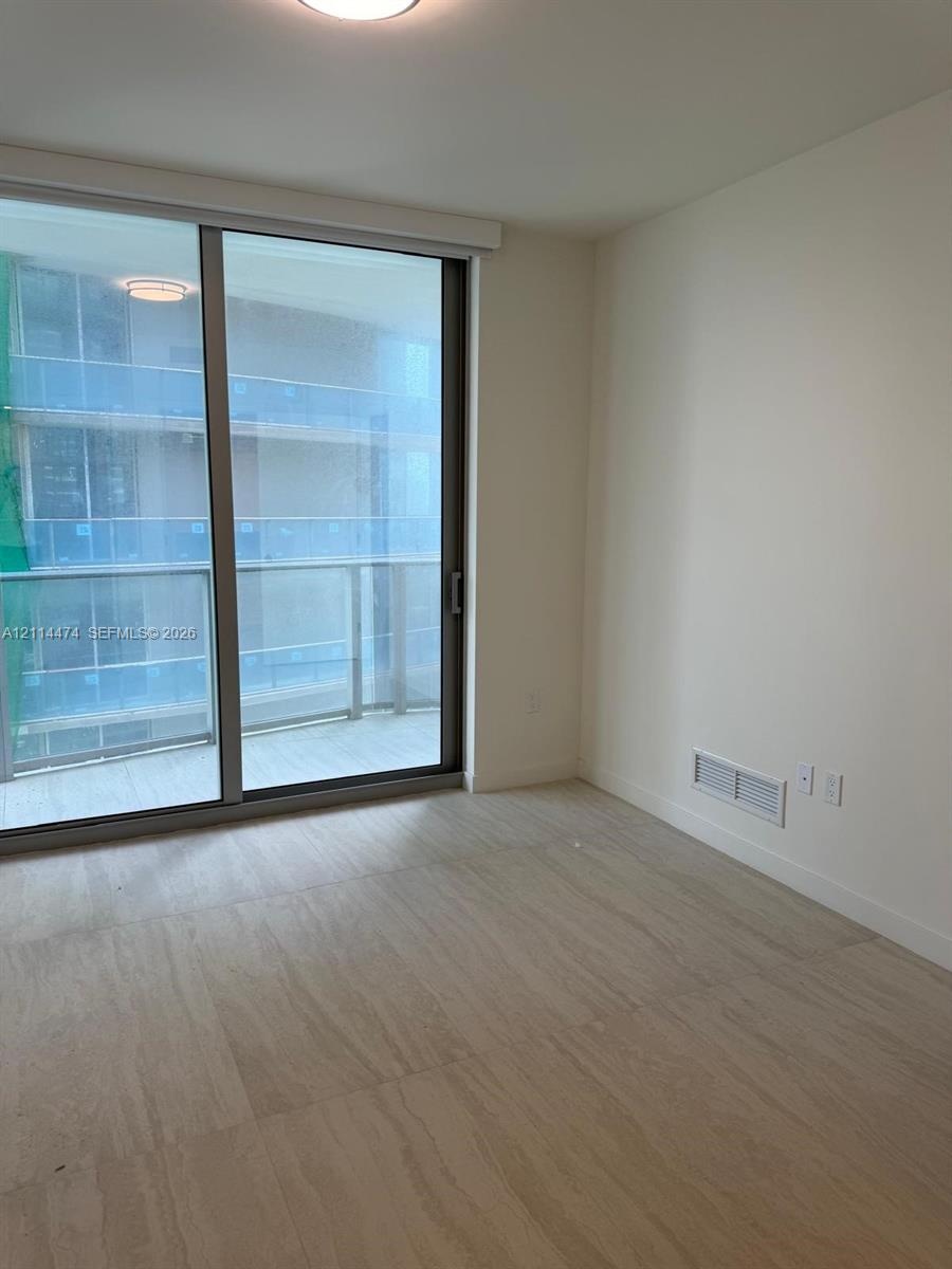 Floor-to-ceiling sliding glass door, private balcony with glass railing, and wood-finish flooring