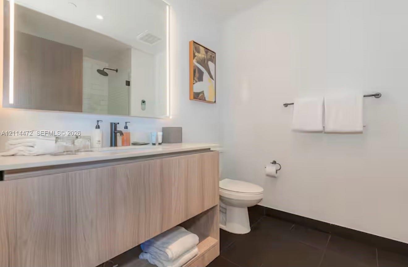Floating vanity with wood-finish cabinetry and light-toned countertop, large rectangular mirror with integrated LED lighting, matte black fixtures, an
