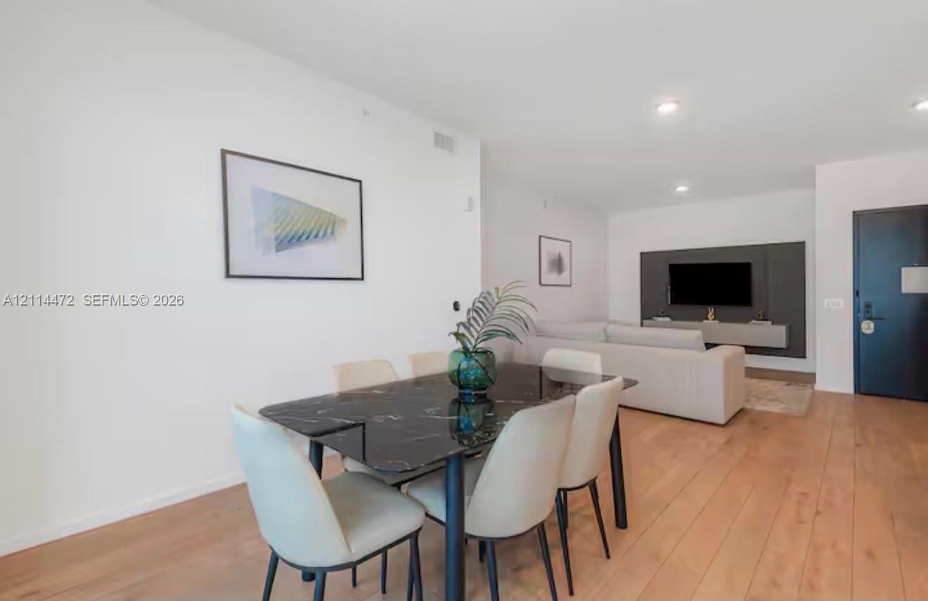 Open-concept interior featuring wood-finish flooring, recessed lighting, and a dark accent wall with a wall-mounted media console