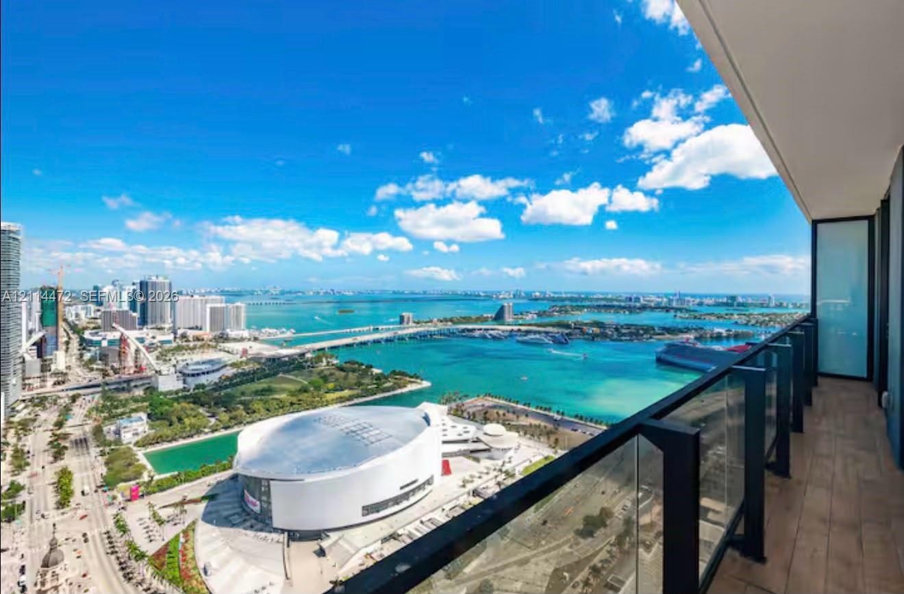 Covered balcony featuring wood-finish flooring and a glass railing with black metal framing, showcasing an expansive waterfront and city skyline panor