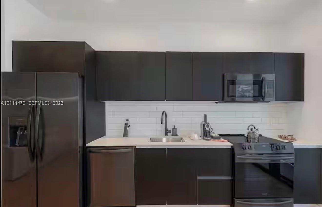 Modern kitchen featuring flat-panel cabinetry, a white subway tile backsplash, light-toned countertops, a stainless steel undermount sink, and matte b