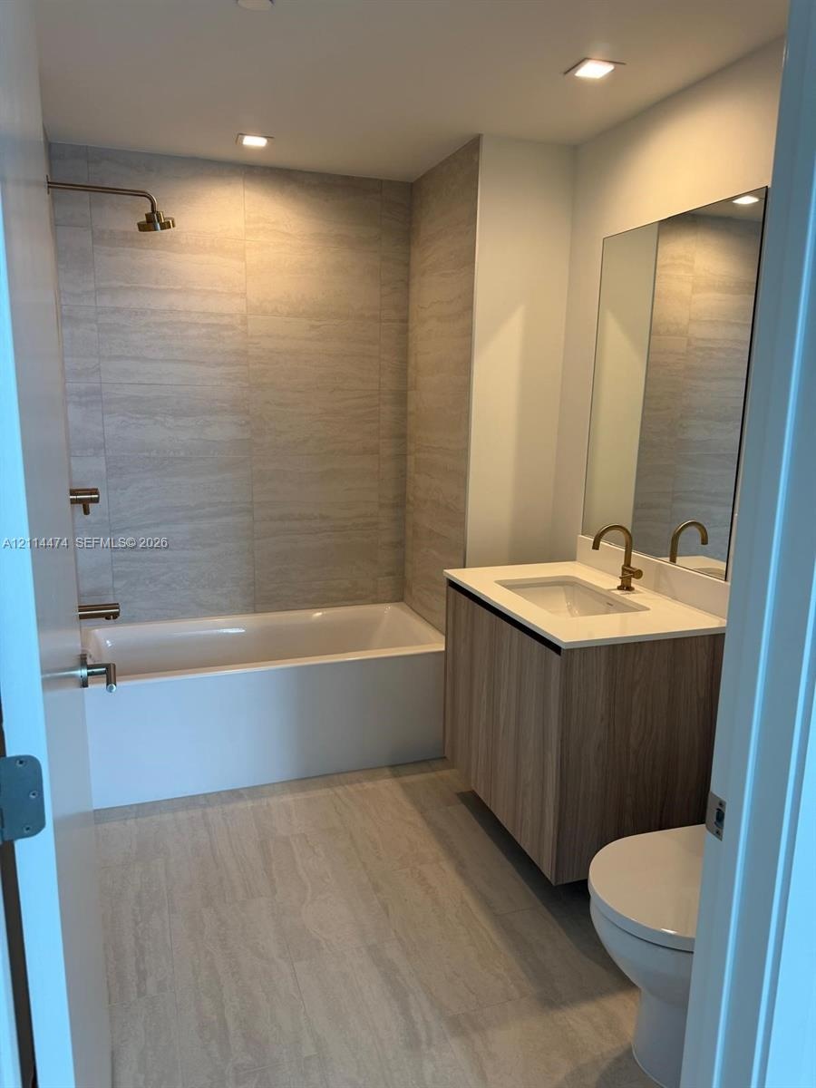 Bathroom featuring a floating vanity with wood-finish cabinetry, a white countertop with an integrated sink, a rectangular wall-mounted mirror, floor-