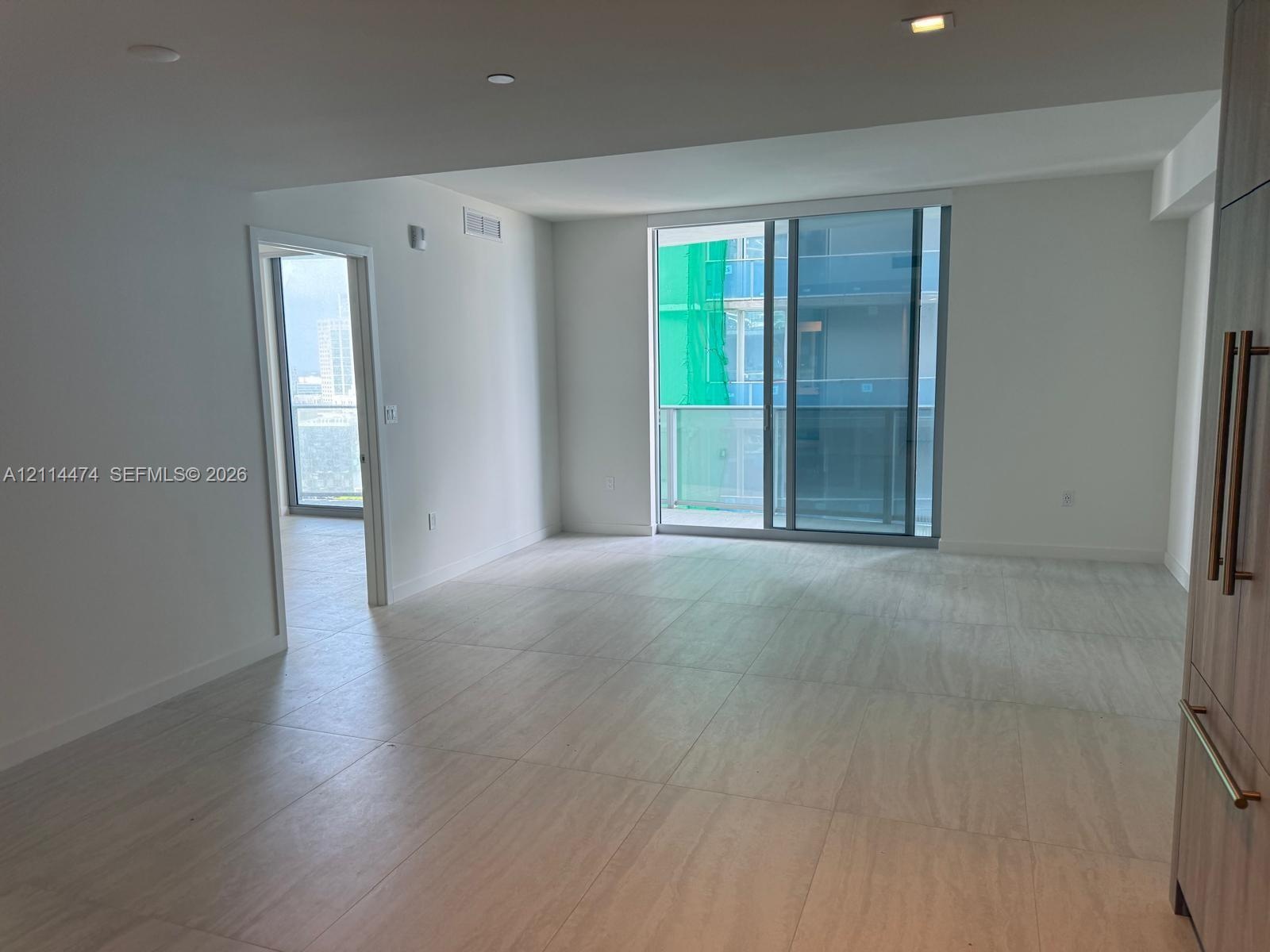 Open-concept living space featuring neutral large-format tile flooring, floor-to-ceiling sliding glass doors, built-in cabinetry with metallic pulls, 