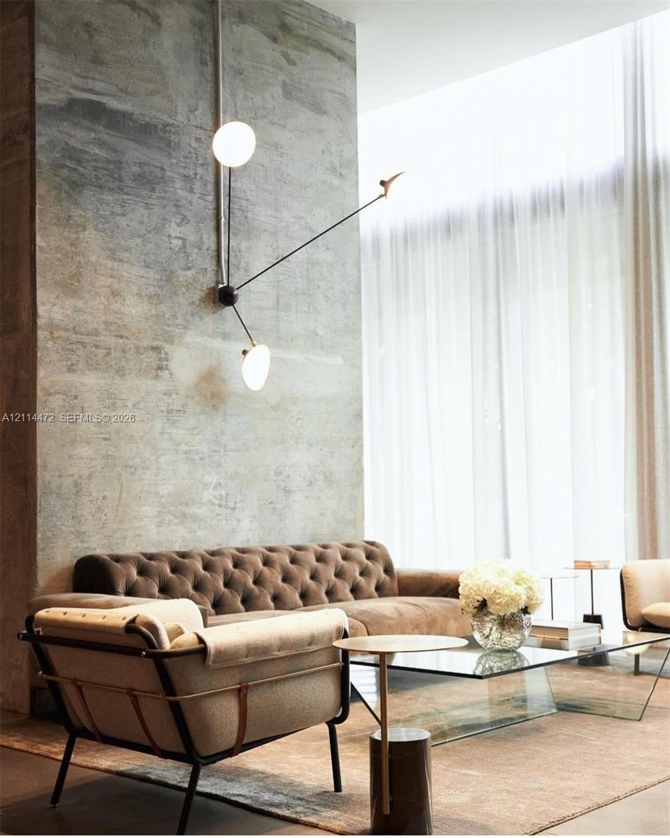 Exposed concrete accent wall with floor-to-ceiling height, multi-arm wall-mounted light fixture with globe bulbs, and full-height window drapery
