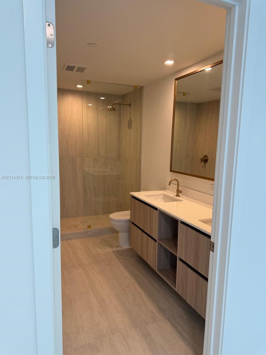 Bathroom featuring a floating vanity with wood-finish cabinetry, solid-surface countertop with dual under-mount sinks, gold-tone hardware, and a walk-