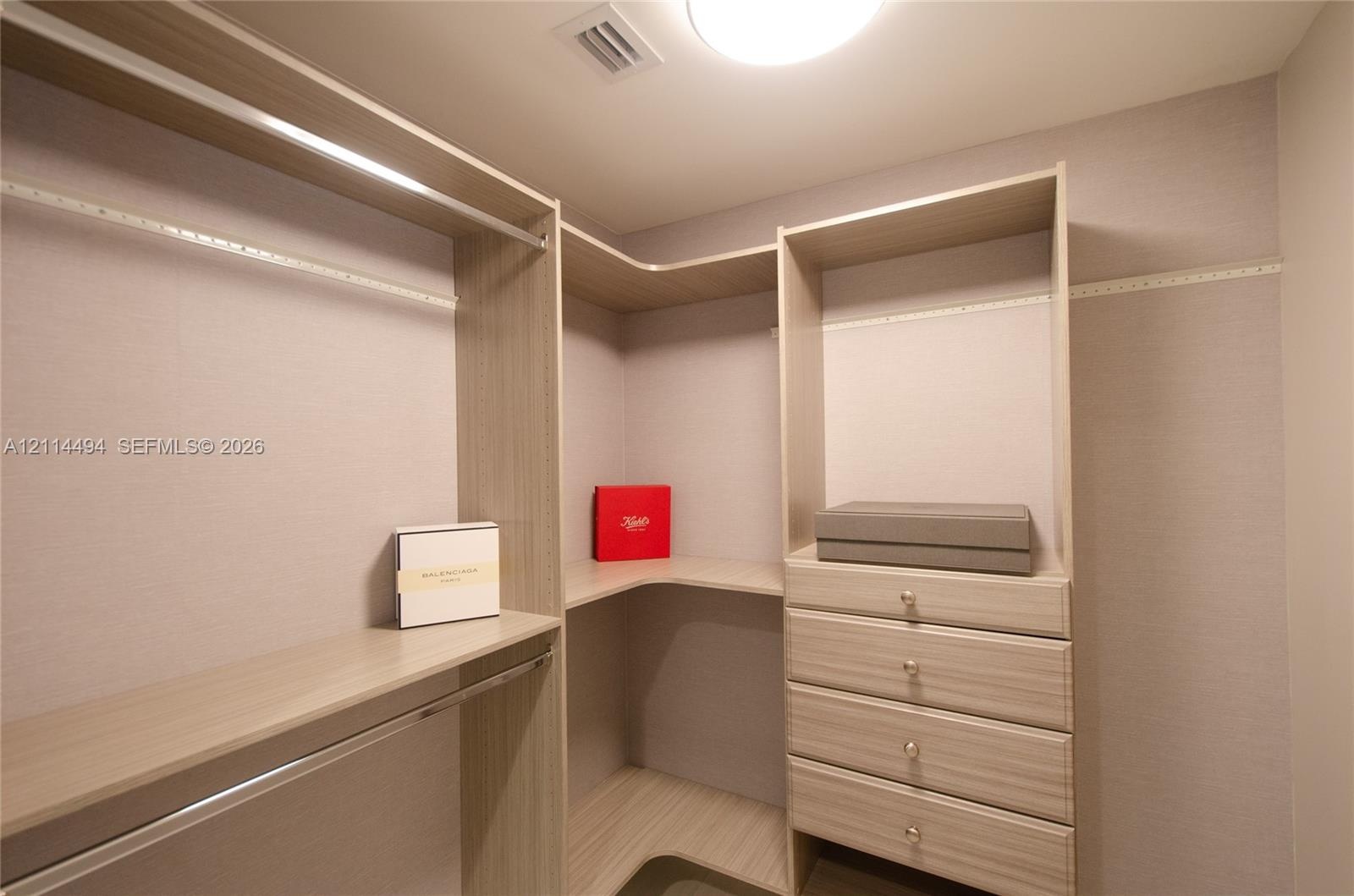 Walk-in closet featuring light wood-finish shelving, integrated hanging rods, and a four-drawer built-in cabinet unit with metallic pulls