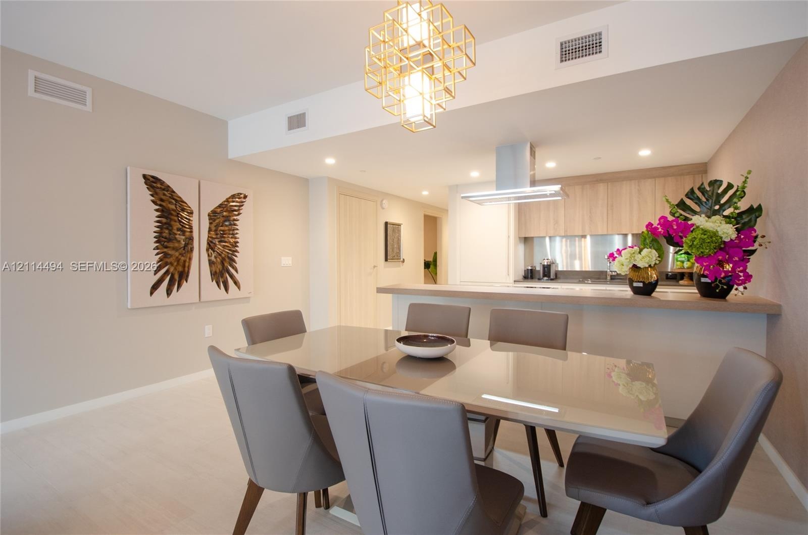 Kitchen featuring light wood-finish cabinetry, a stainless steel range hood, a breakfast bar, and a geometric gold-tone pendant light