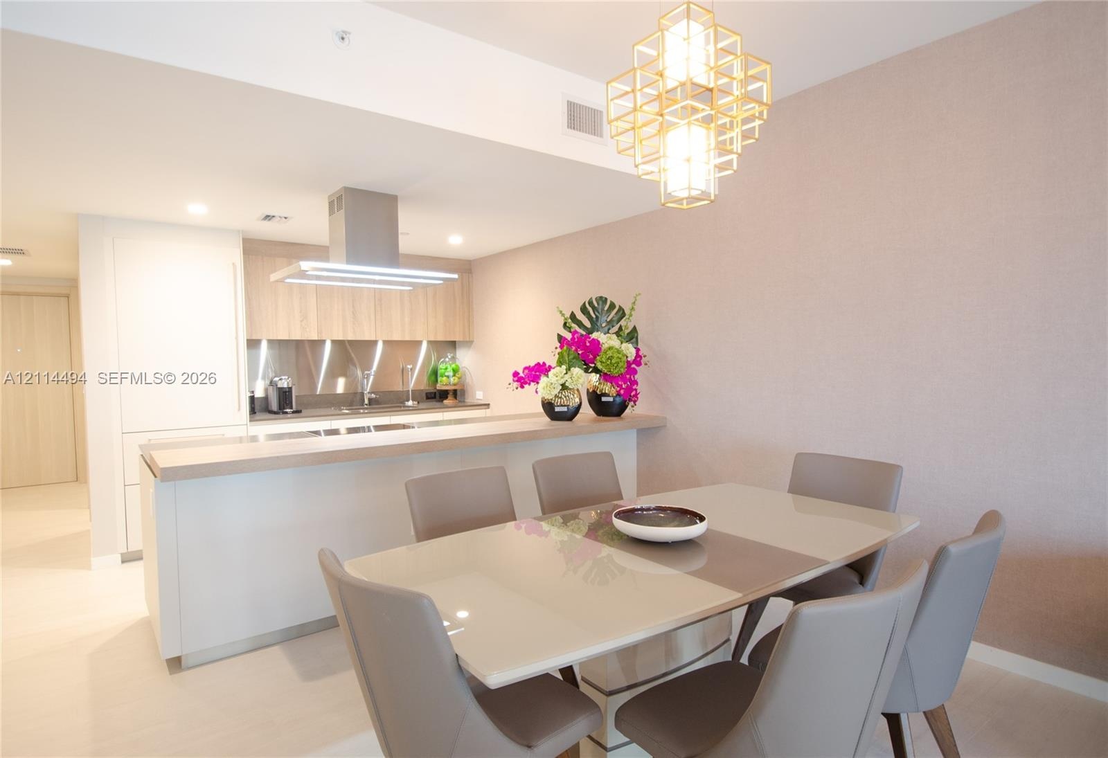 Kitchen featuring light-toned cabinetry, a peninsula with a solid-surface countertop, stainless steel range hood, and a geometric gold-tone pendant li