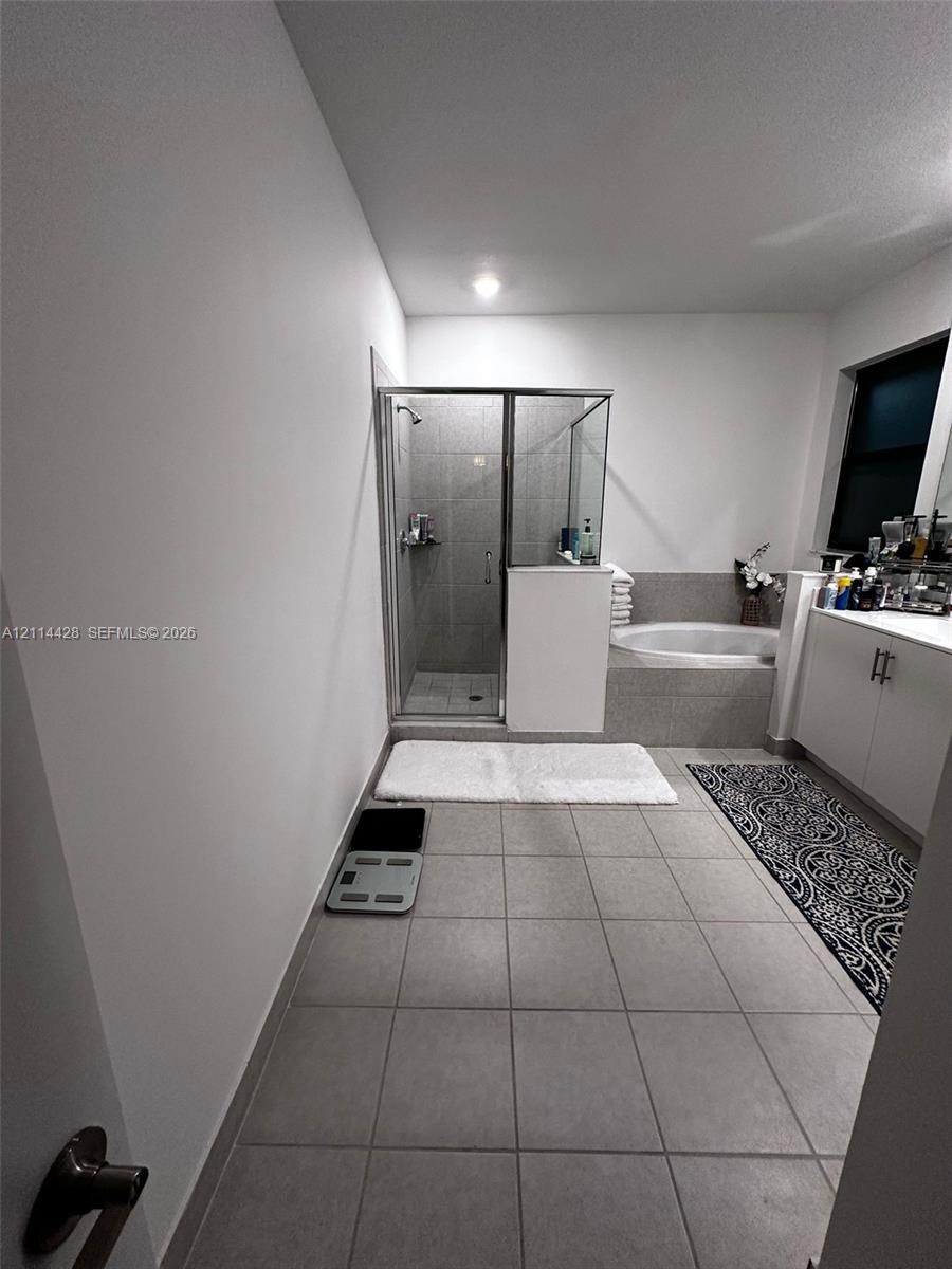 Bathroom featuring large-format tile flooring, a walk-in shower with a glass enclosure, a built-in soaking tub with tile surround, and a vanity with w