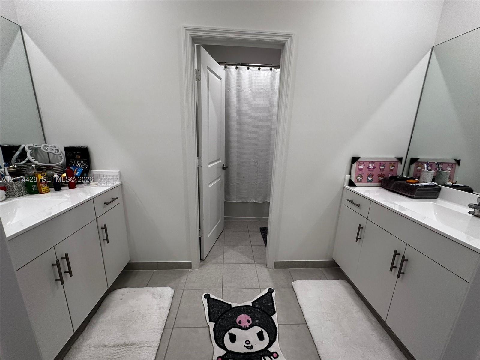 Dual vanity area featuring white cabinetry, light-toned stone-finish countertops, undermount sinks, wall-to-wall mirrors, and tile flooring