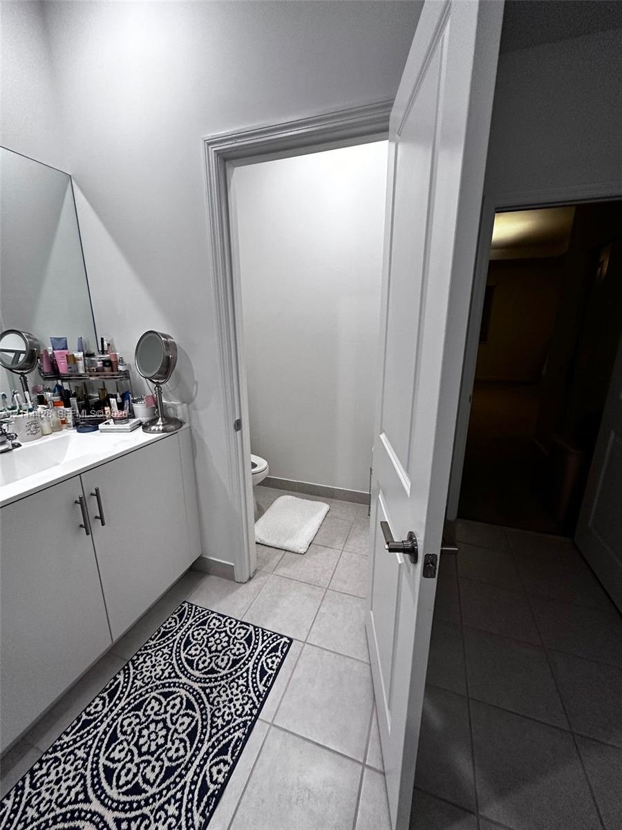 White vanity cabinet with a solid surface countertop, integrated sink, and modern metal hardware, complemented by tile flooring and a panel door