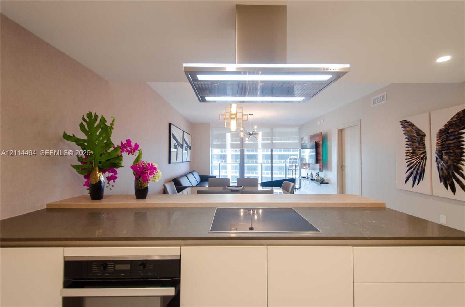Kitchen peninsula featuring a stone countertop, built-in cooktop, and elevated wood-finish breakfast bar, complemented by a stainless steel ceiling-mo