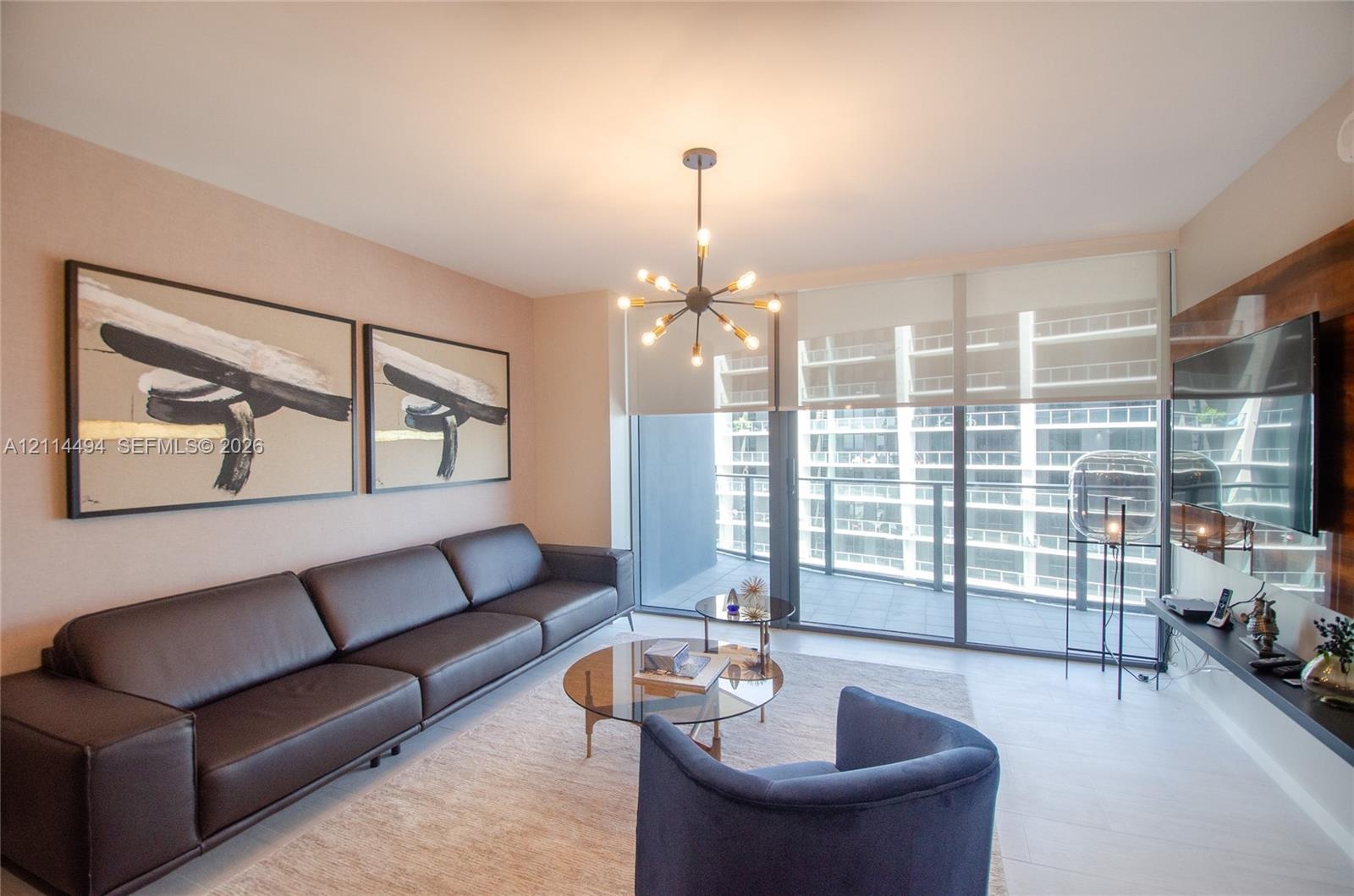 Living area featuring light-toned flooring, floor-to-ceiling glass doors, a contemporary multi-arm sputnik-style chandelier, and a wood-finish wall pa