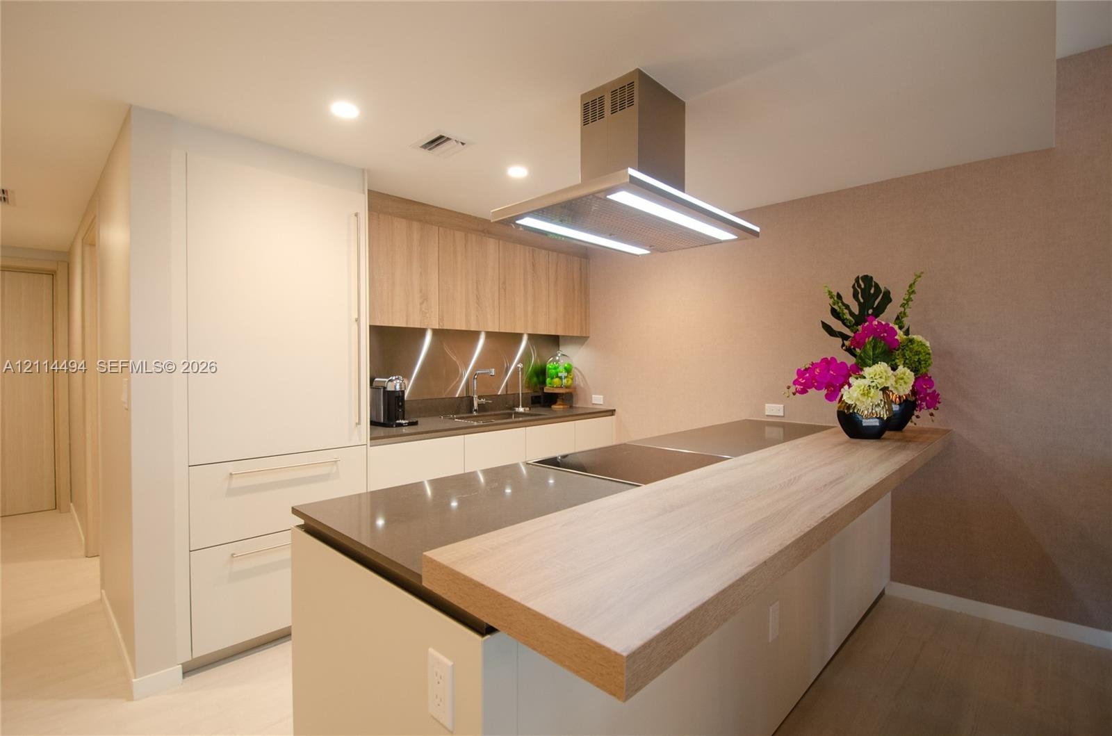 Kitchen featuring custom cabinetry with wood-finish and solid-color flat-panel doors, stone-composite countertops, integrated appliances, and a stainl