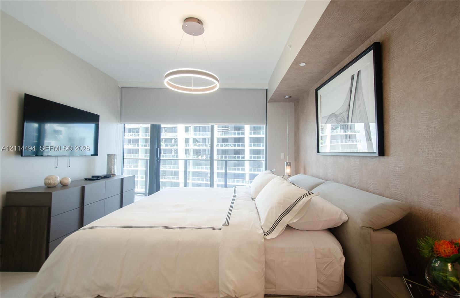 Floor-to-ceiling windows with roller shades, recessed cove lighting, circular LED chandelier, and textured wall finish