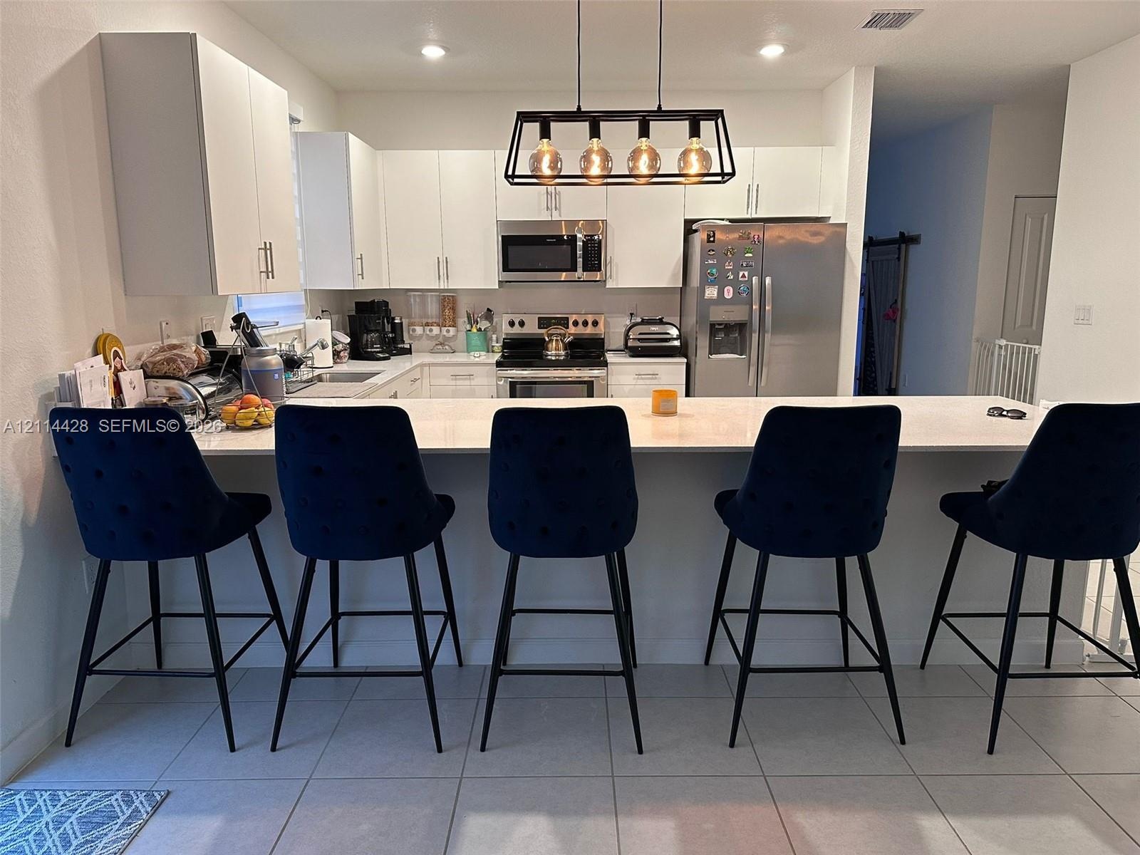Kitchen featuring white cabinetry, solid-surface countertops with an integrated breakfast bar, stainless steel appliances, and rectangular-tile floori