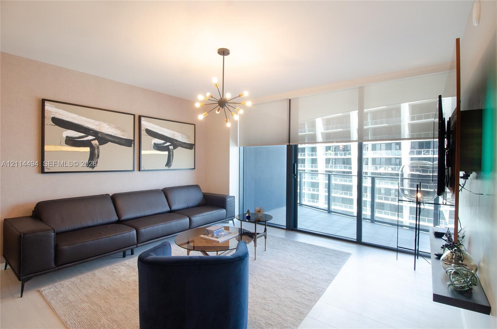 Floor-to-ceiling sliding glass doors, private balcony, contemporary multi-arm chandelier, and light-toned tile flooring