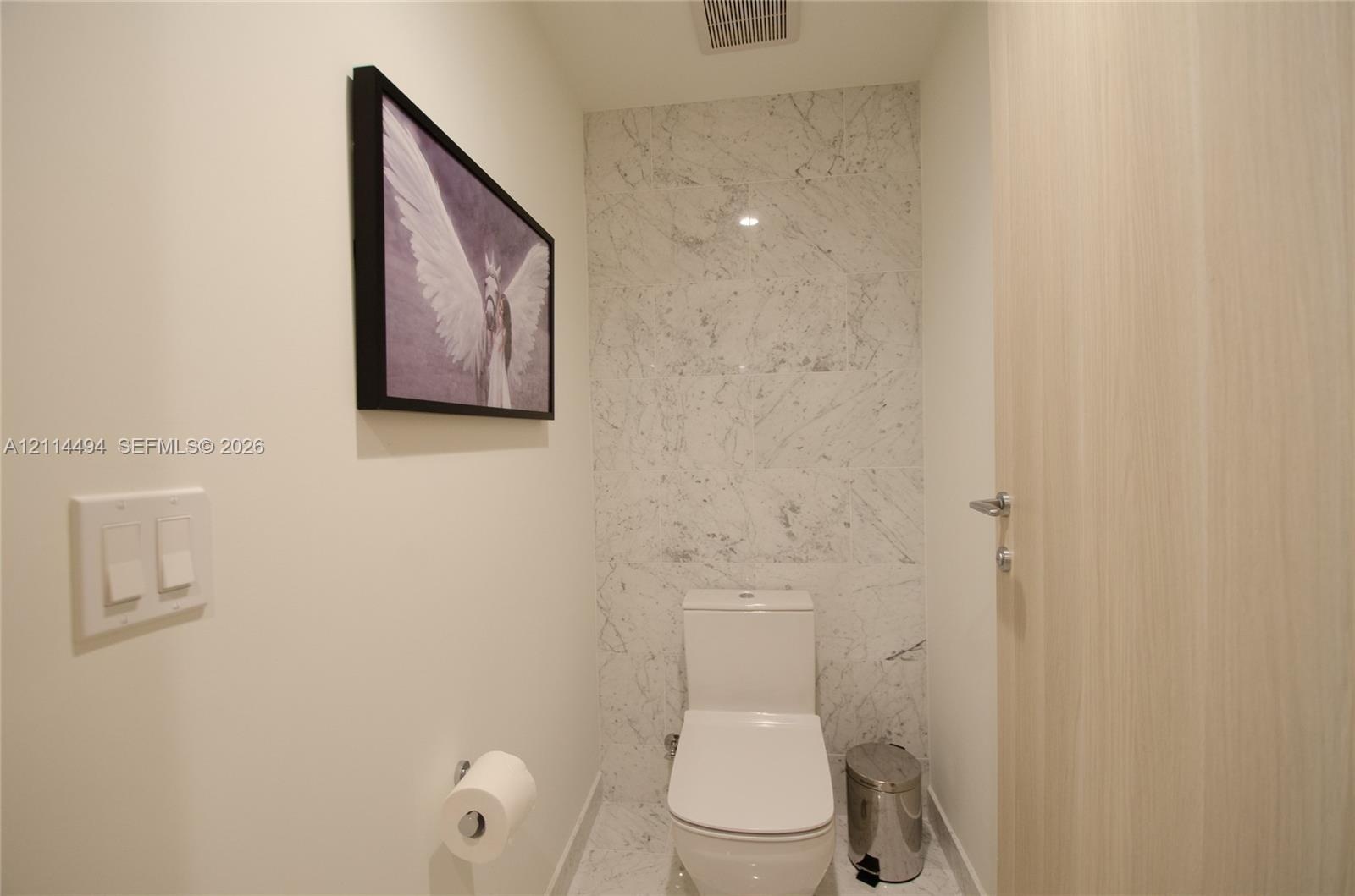 Powder room featuring a stone-finish tile accent wall, stone-finish flooring, dual-flush elongated toilet, and a light-toned wood-finish door