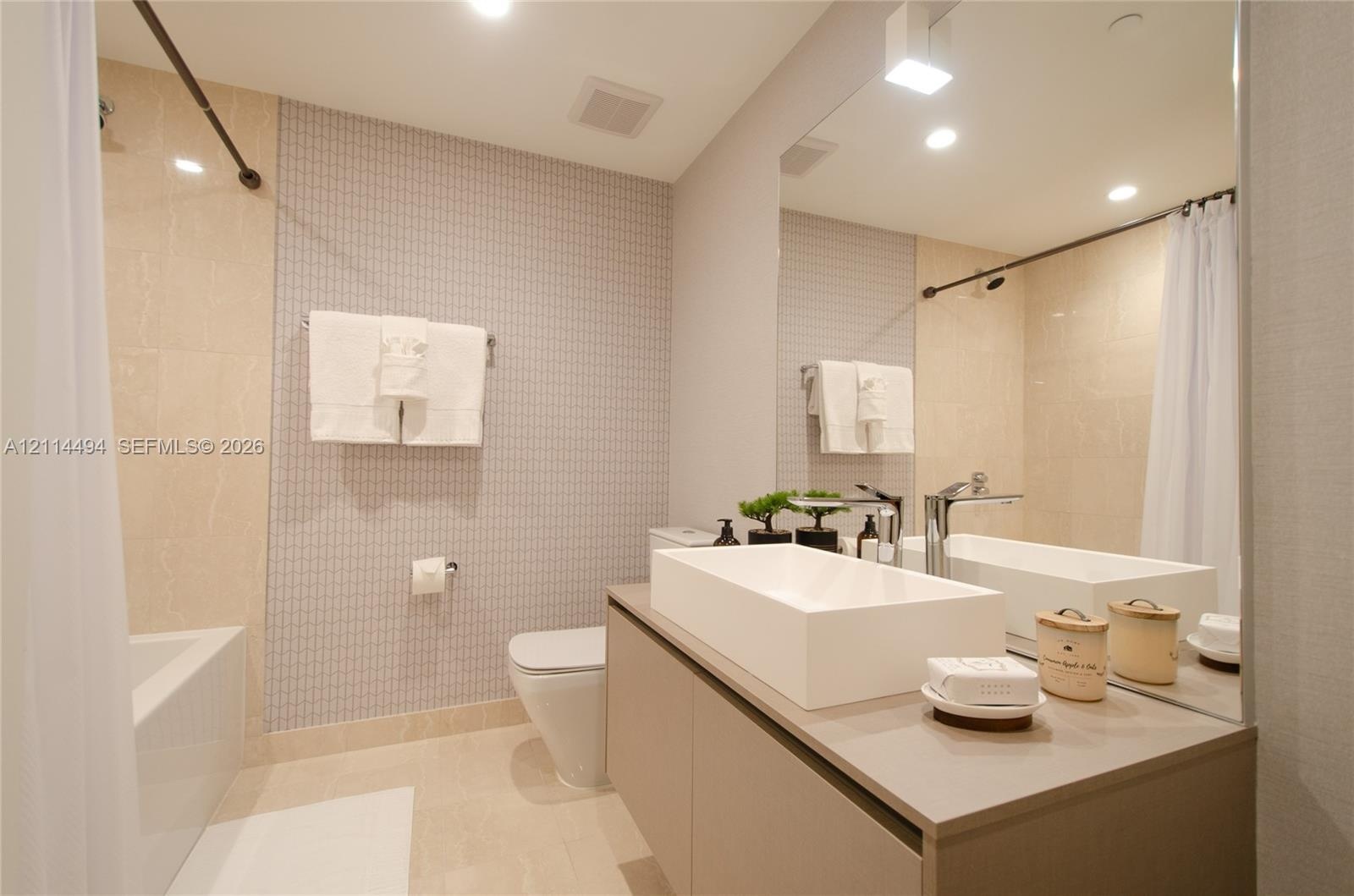 Floating vanity featuring a rectangular vessel sink and polished chrome faucet, paired with a large wall-mounted mirror, mosaic tile wall accents, and