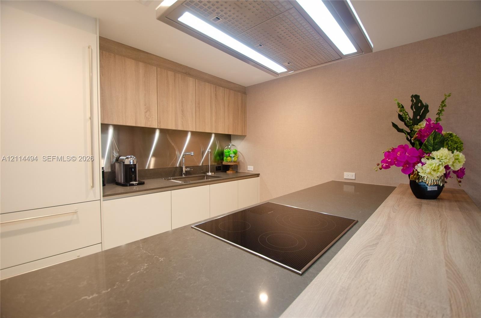 Kitchen featuring flat-panel cabinetry, stone countertops, metallic backsplash, integrated induction cooktop, and flush-mount overhead ventilation