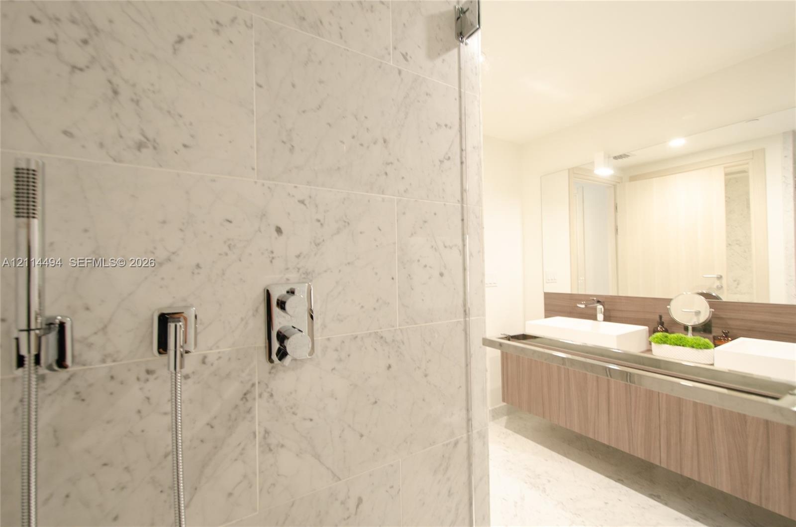 Shower area featuring large-format natural stone wall tile, chrome handheld shower fixture, and wall-mounted chrome controls, paired with a floating w