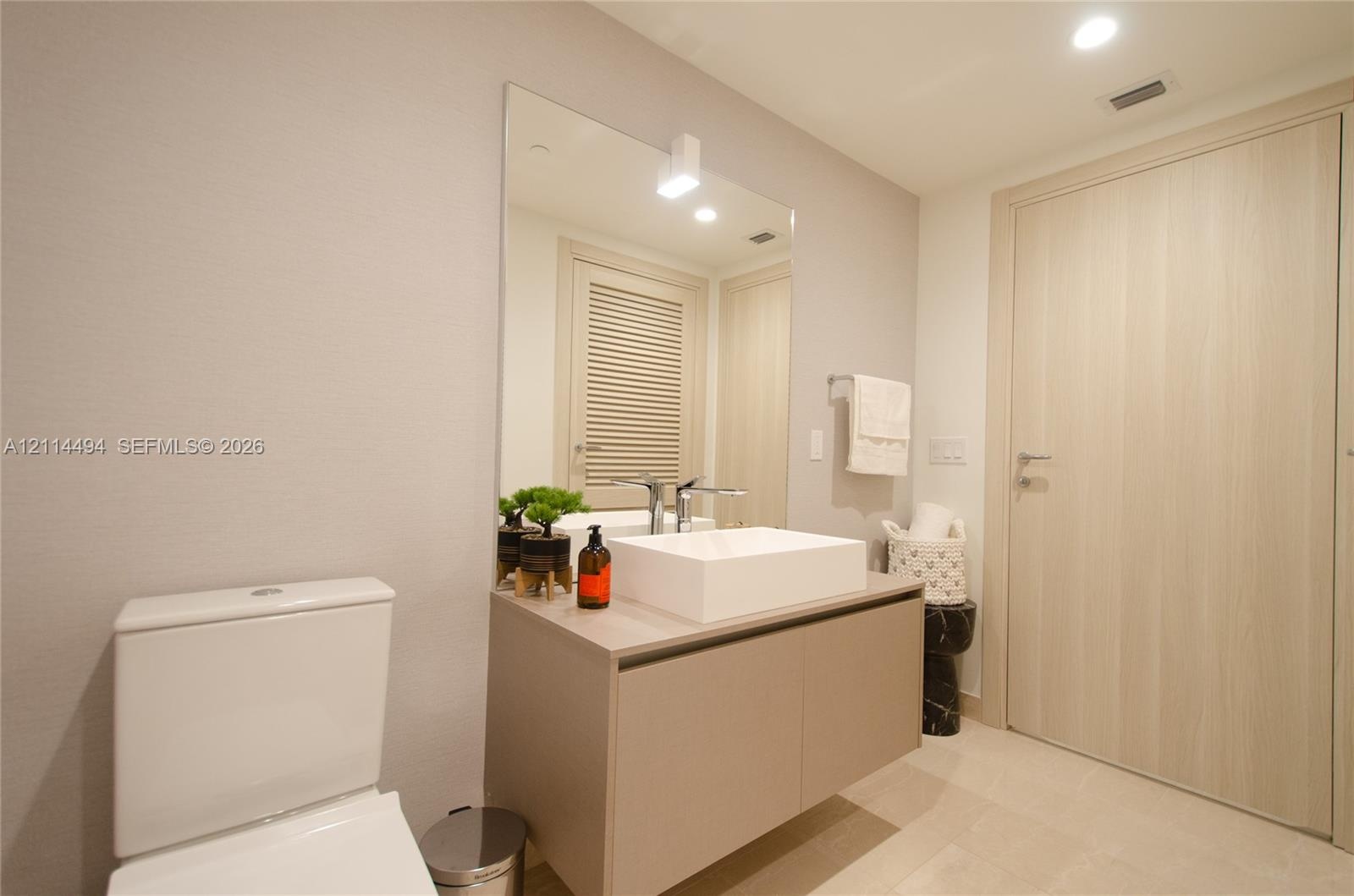 Floating vanity featuring a flat-panel cabinet, rectangular vessel sink, and chrome faucet, complemented by a large frameless wall mirror and wood-fin