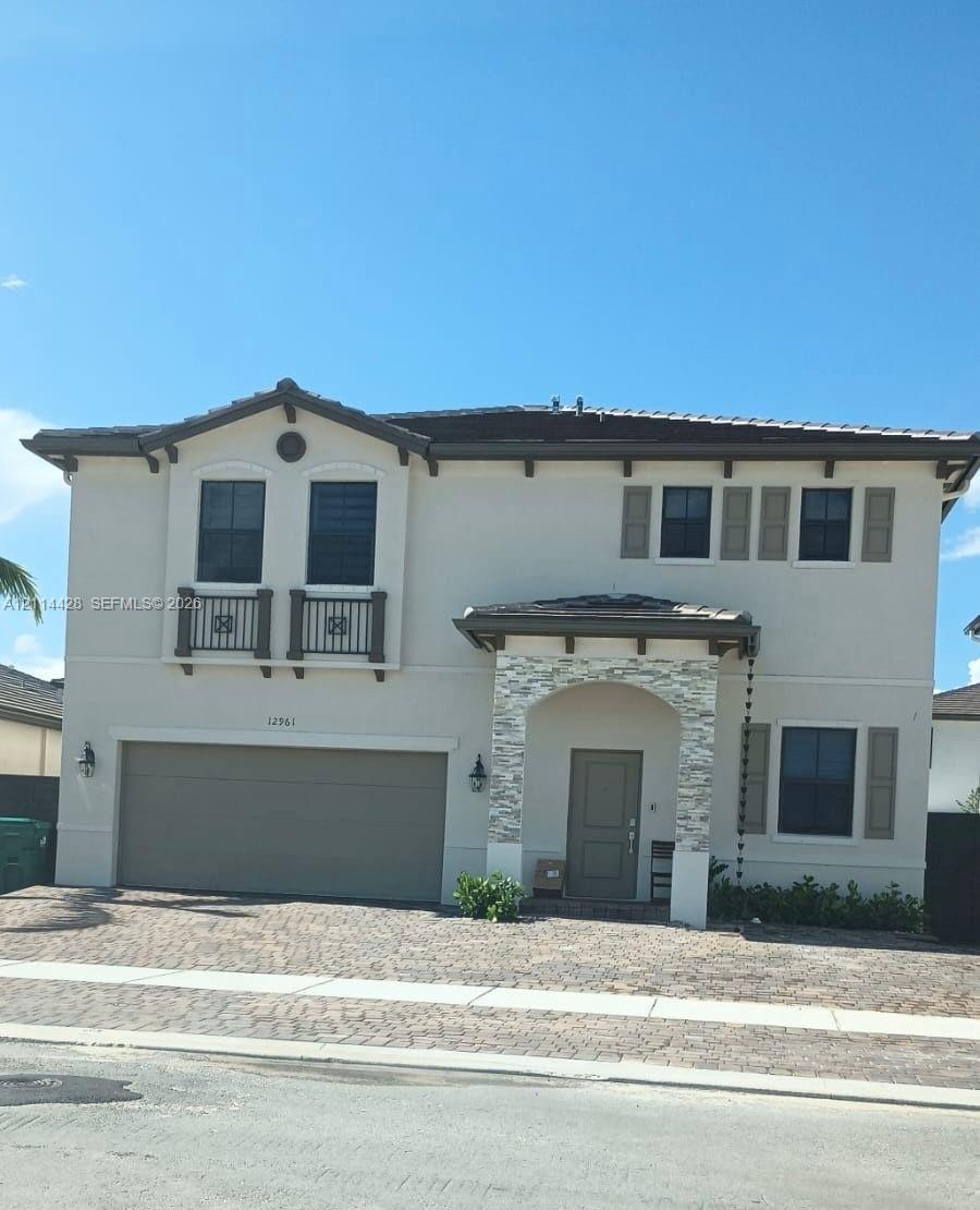 Two-story exterior featuring light-toned stucco, decorative stacked stone facade accents, two faux-balconies with railing detail, multi-pane windows w