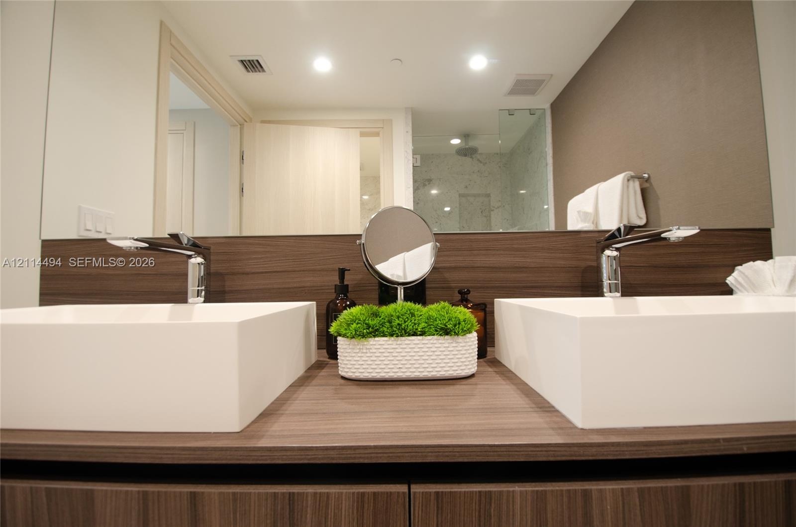 Dual rectangular vessel sinks atop a wood-finish vanity with a matching backsplash, polished chrome faucets, and a large integrated mirror
