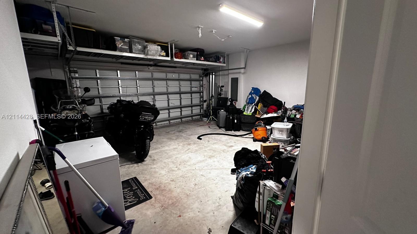 Garage interior featuring a sectional metal garage door, concrete flooring, and elevated wall-mounted steel shelving units