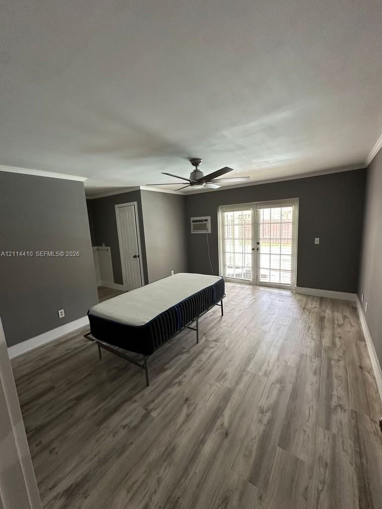 Wood-finish flooring, neutral wall tones, multi-light French doors, ceiling fan, and wall-mounted air conditioning unit