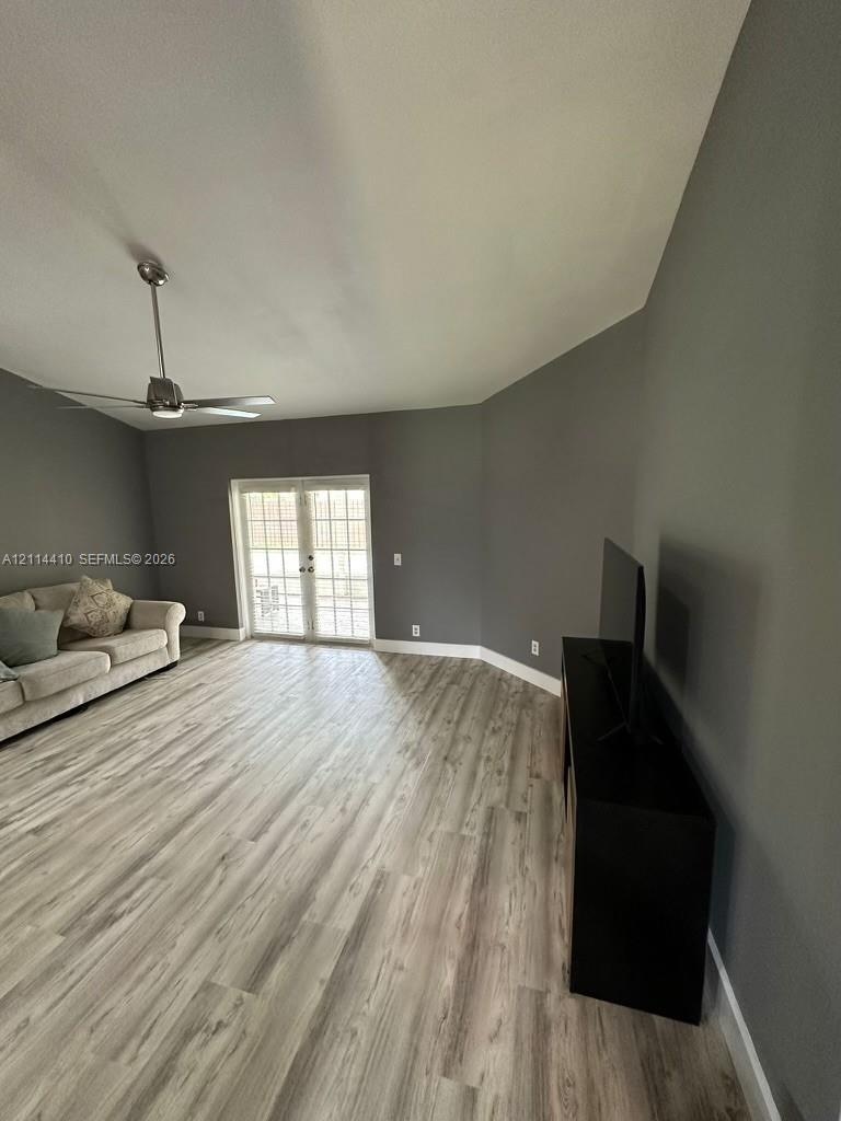 Living area featuring vaulted ceilings, wood-finish flooring, neutral wall paint, a ceiling fan, and double-pane glass French doors