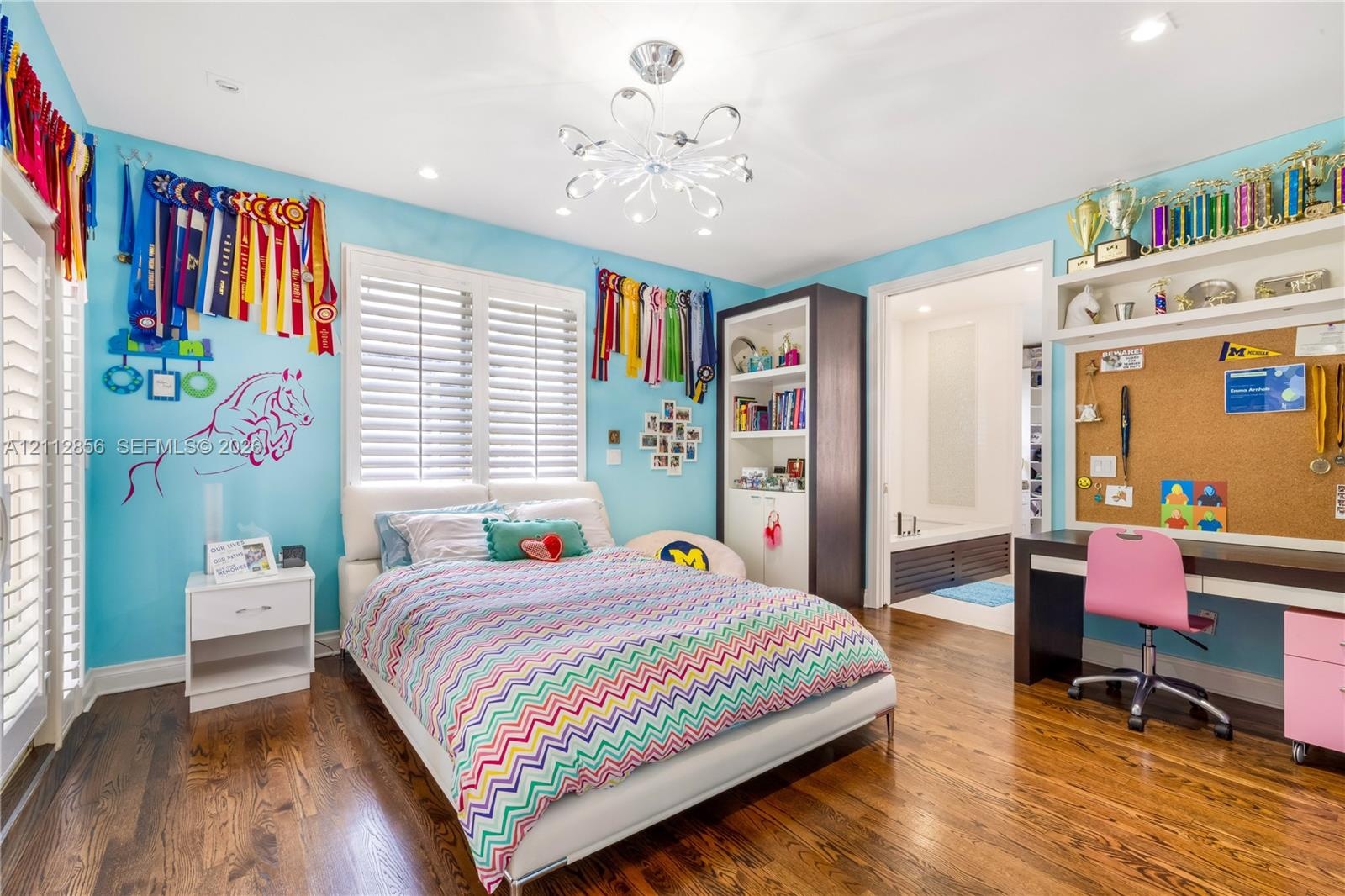 Hardwood flooring, multi-tier decorative ceiling light fixture, plantation shutters, built-in floor-to-ceiling cabinetry, and integrated desk with ove