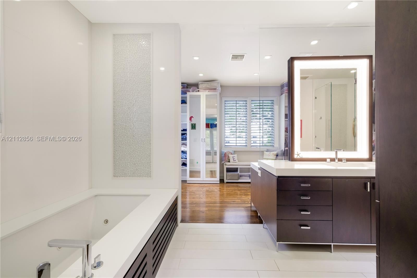 Contemporary bathroom featuring a deep-soaking tub with a tiled surround, custom dark-finish vanity cabinetry with a stone countertop, an integrated L