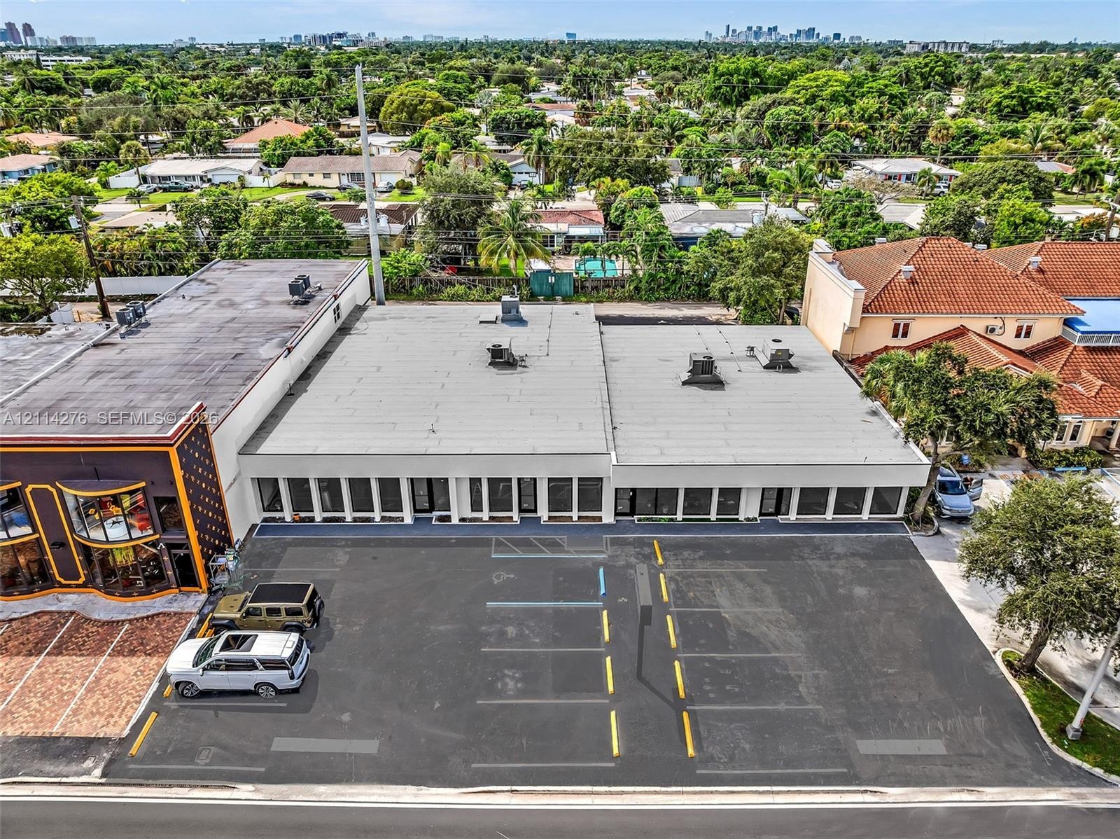 Commercial property exterior featuring a dedicated asphalt parking lot with marked stalls, multiple glass-paneled storefront entrances, and a flat roo