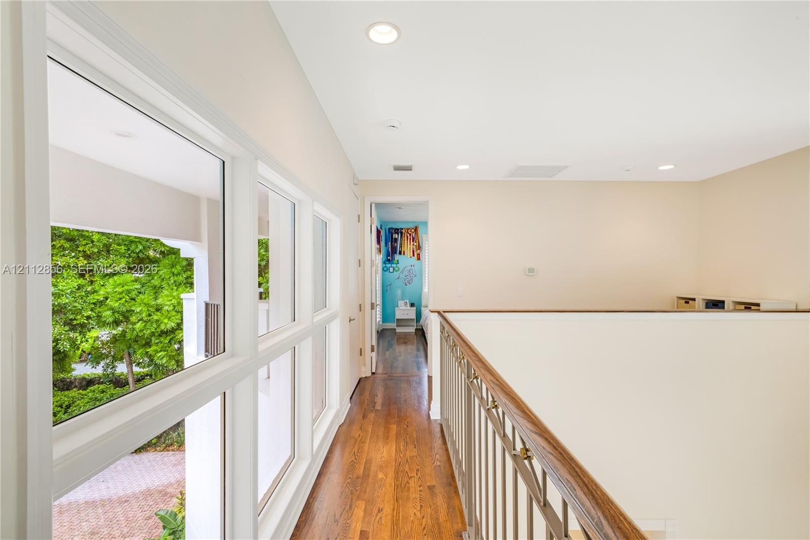 Hallway featuring wood-finish flooring, metal railing with wood-finish handrail, recessed lighting, and large windows