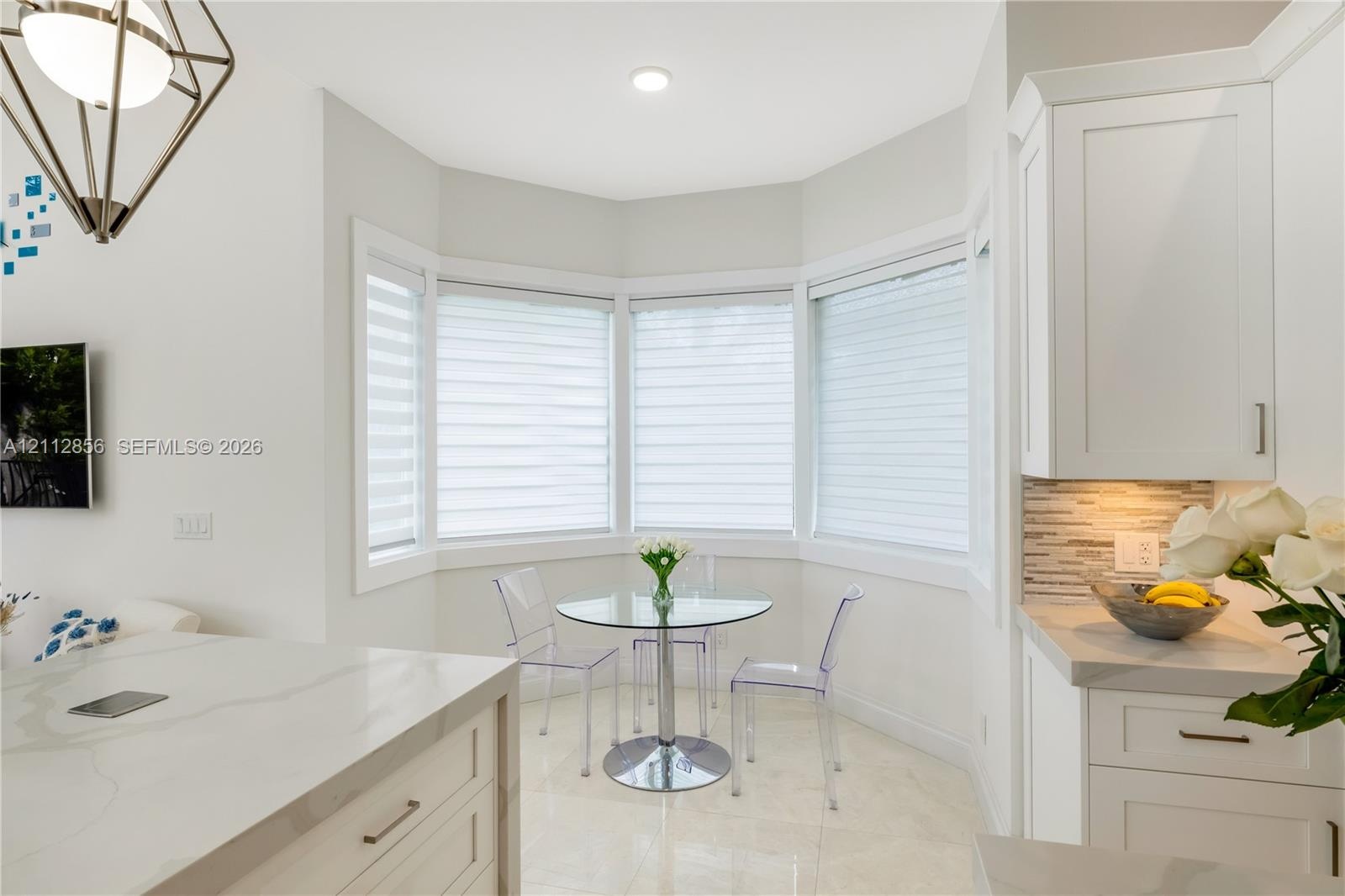 Kitchen nook featuring a bay window, white shaker-style cabinetry, stone-finish countertops, geometric metal pendant lighting, and neutral tile floori