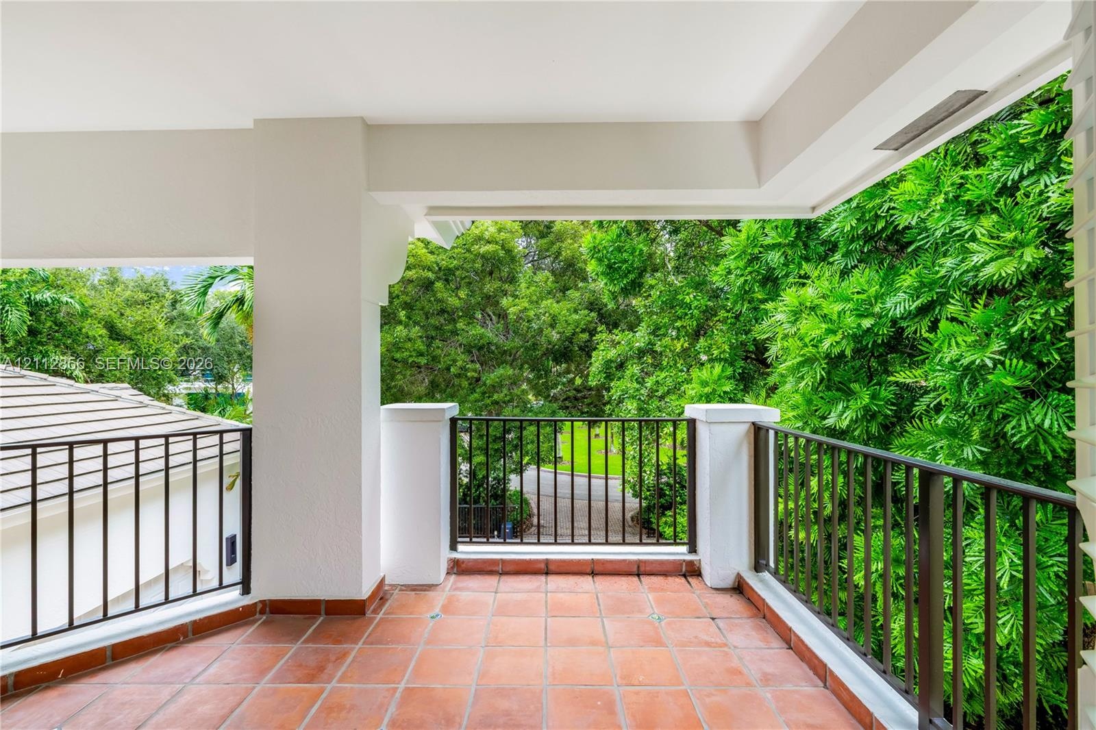 Covered terrace featuring terra cotta tile flooring, metal railing, and concrete pillars