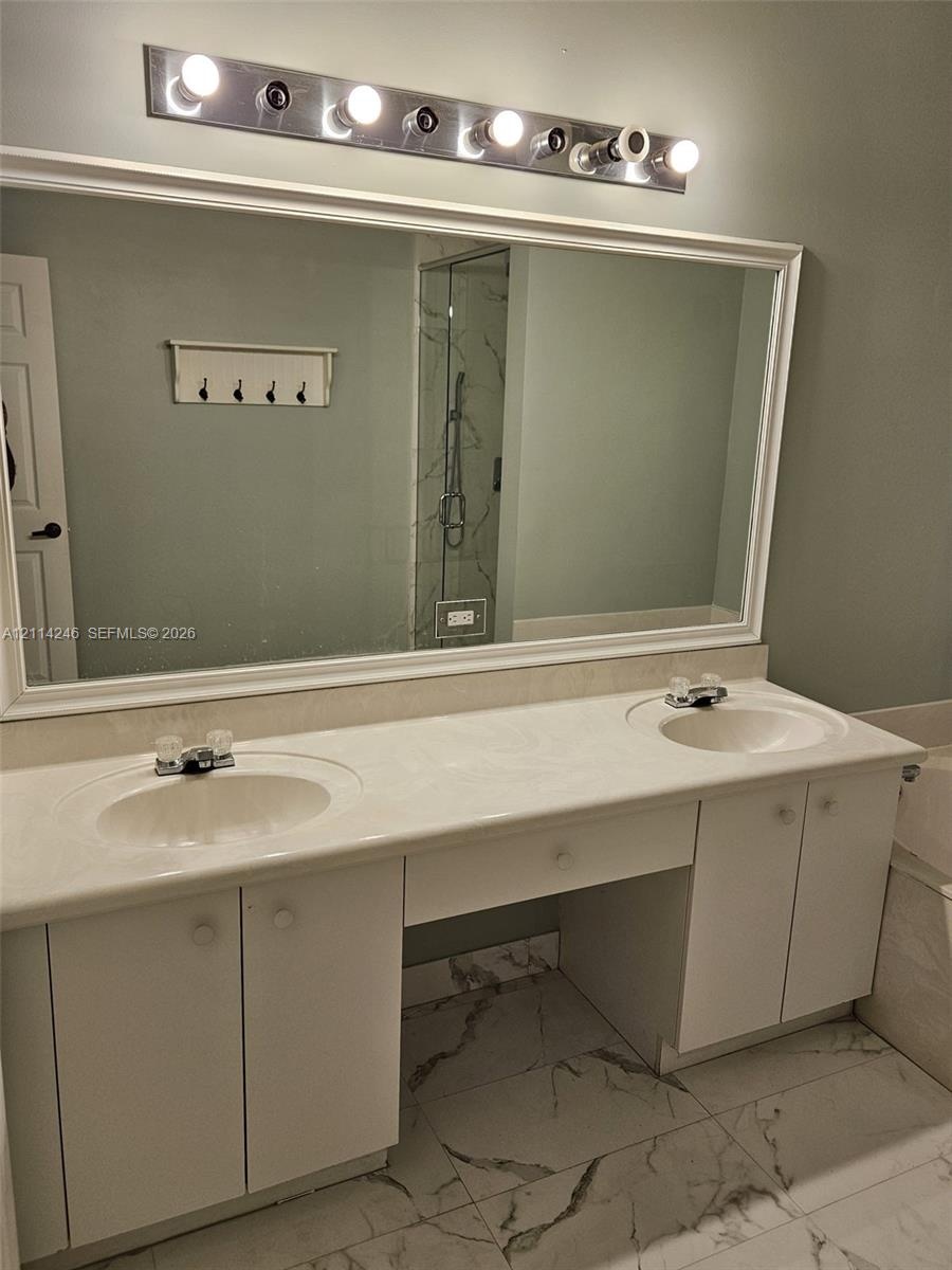 Dual-sink vanity with white cabinetry, integrated stone-finish countertop, full-width mirror, and multi-bulb vanity lighting, accented by large-format