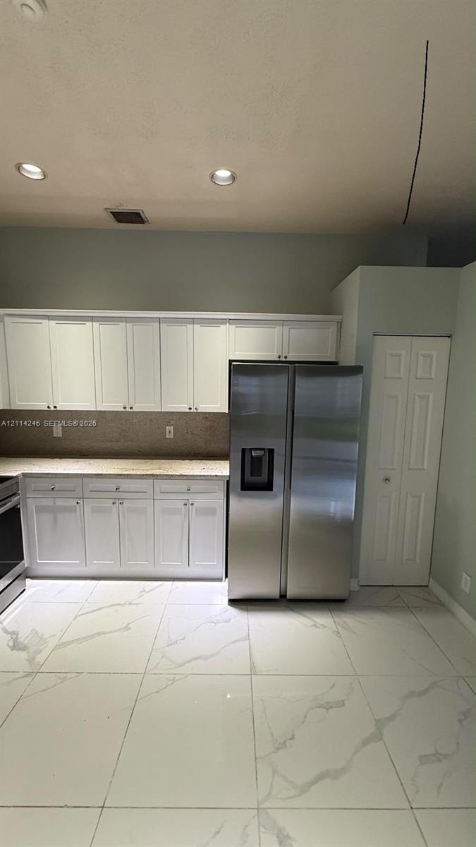 Kitchen featuring white cabinetry, stone-surface countertops, large-format tile flooring, stainless steel side-by-side refrigerator, and recessed ceil