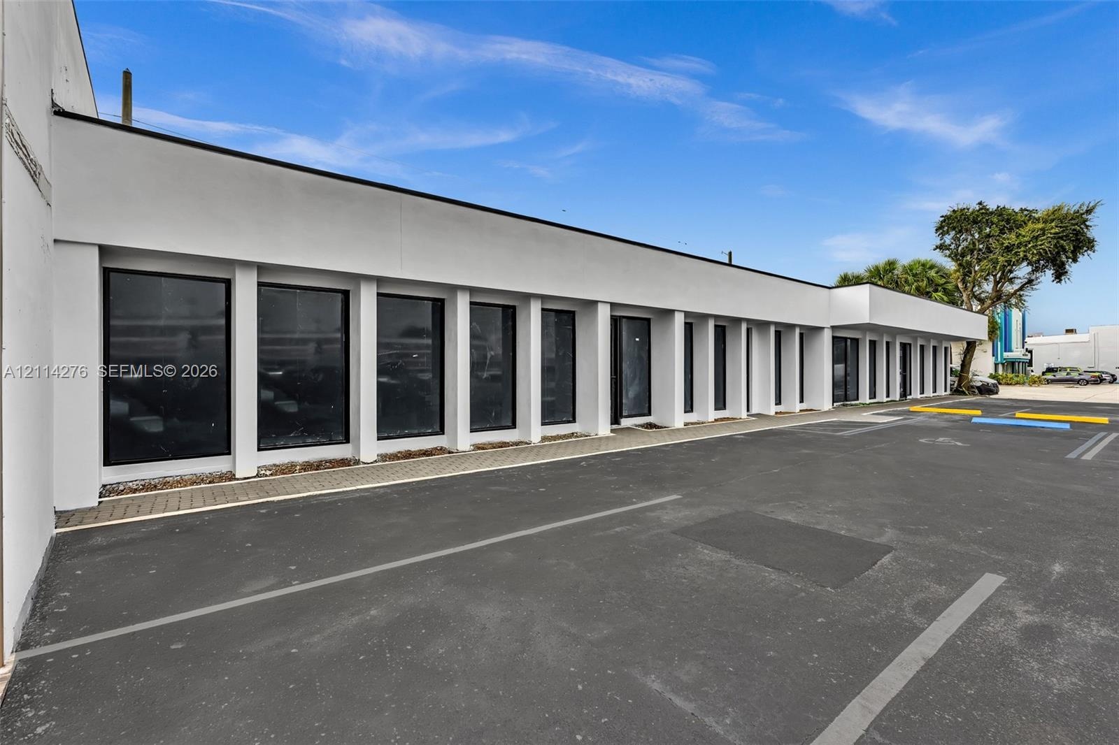 Modern exterior featuring a smooth stucco facade, expansive floor-to-ceiling windows with black framing, rhythmic architectural columns, and an asphal
