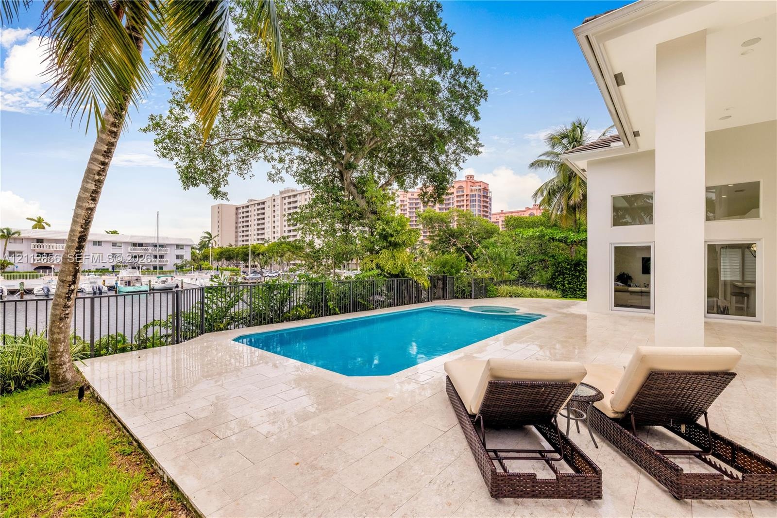 Outdoor terrace featuring natural stone tile flooring, a rectangular swimming pool with integrated spa, and a metal perimeter fence